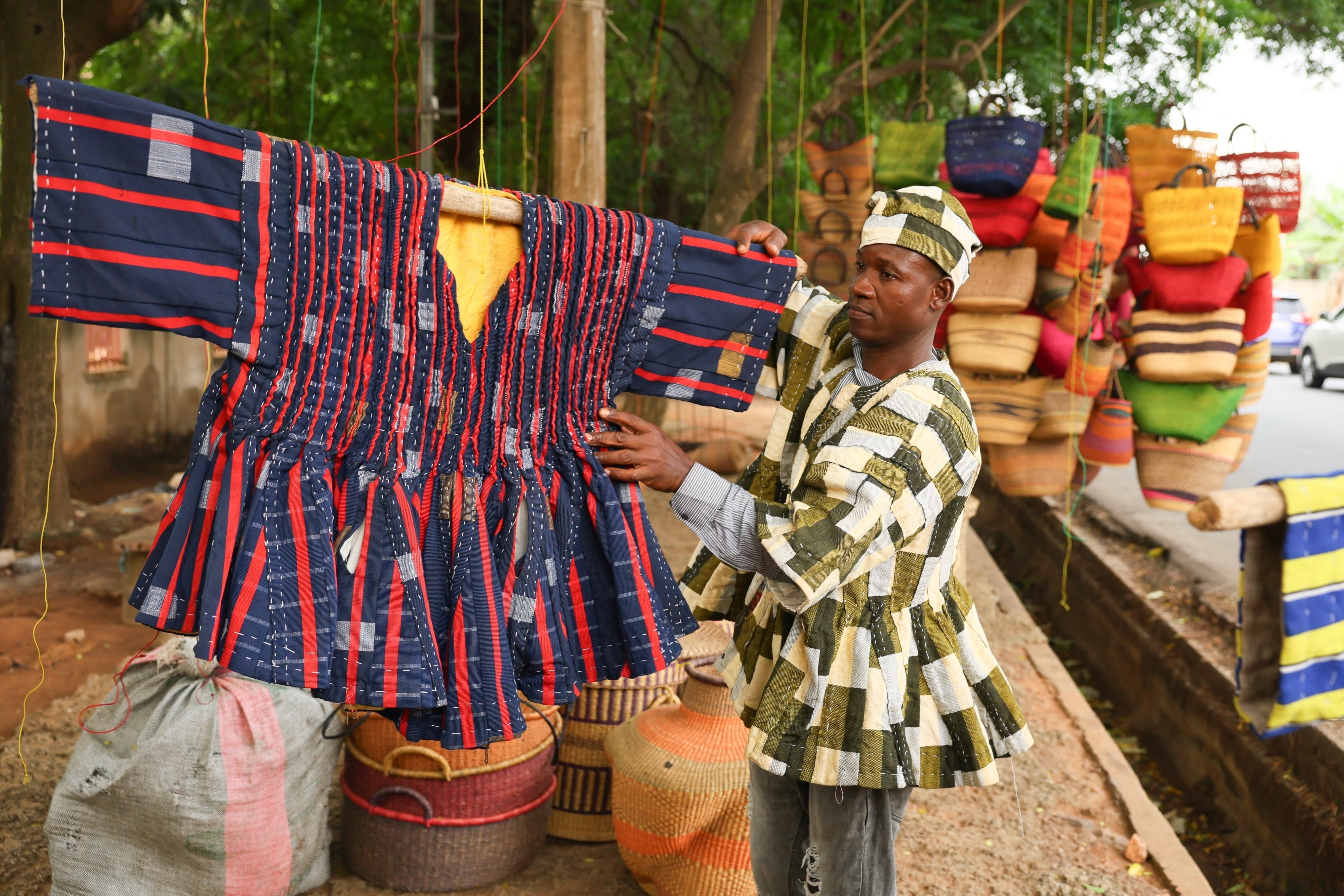 Clement Azaabire hangs traditional fugu garments under a tree on display for sale along a street in Accra, Ghana