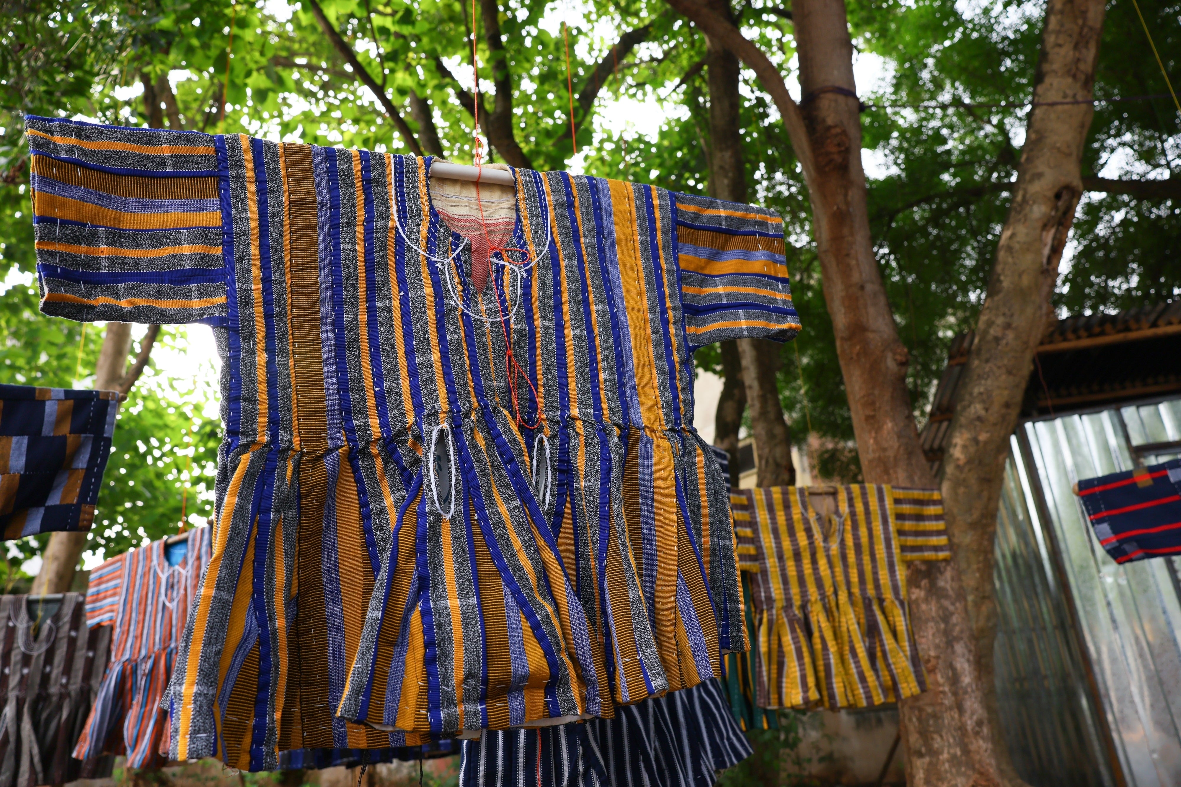 Traditional fugu garments hang under a tree on display for sale along a street in Accra, Ghana