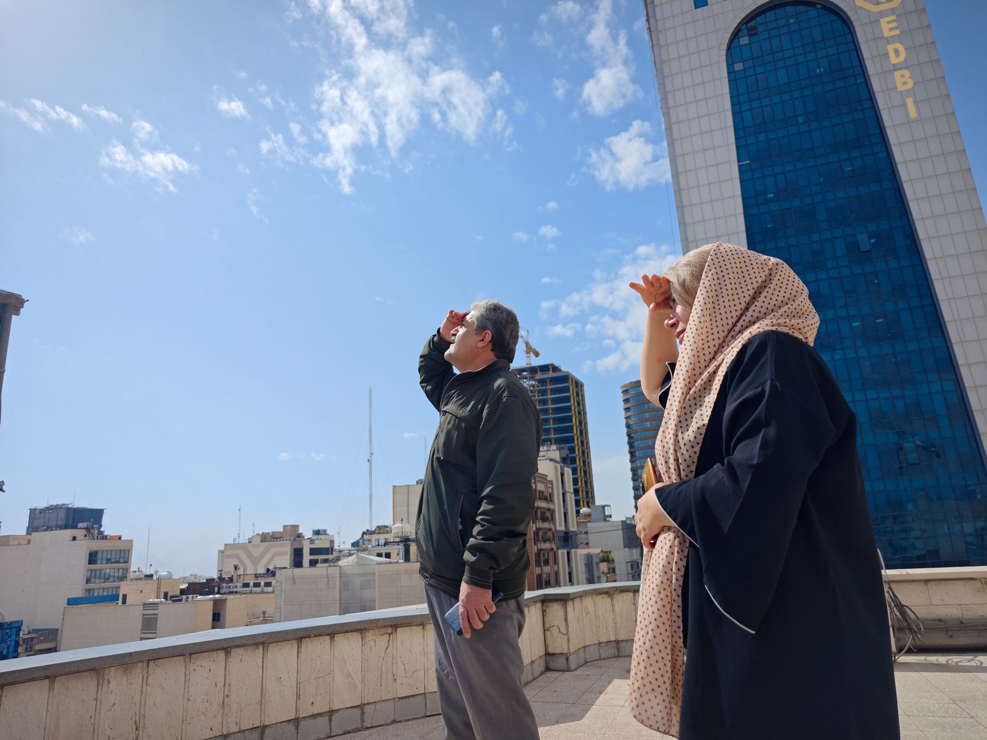 People in Tehran look to the skies from a rooftop amid reports of widespread attacks on Iran by the United States and Israel