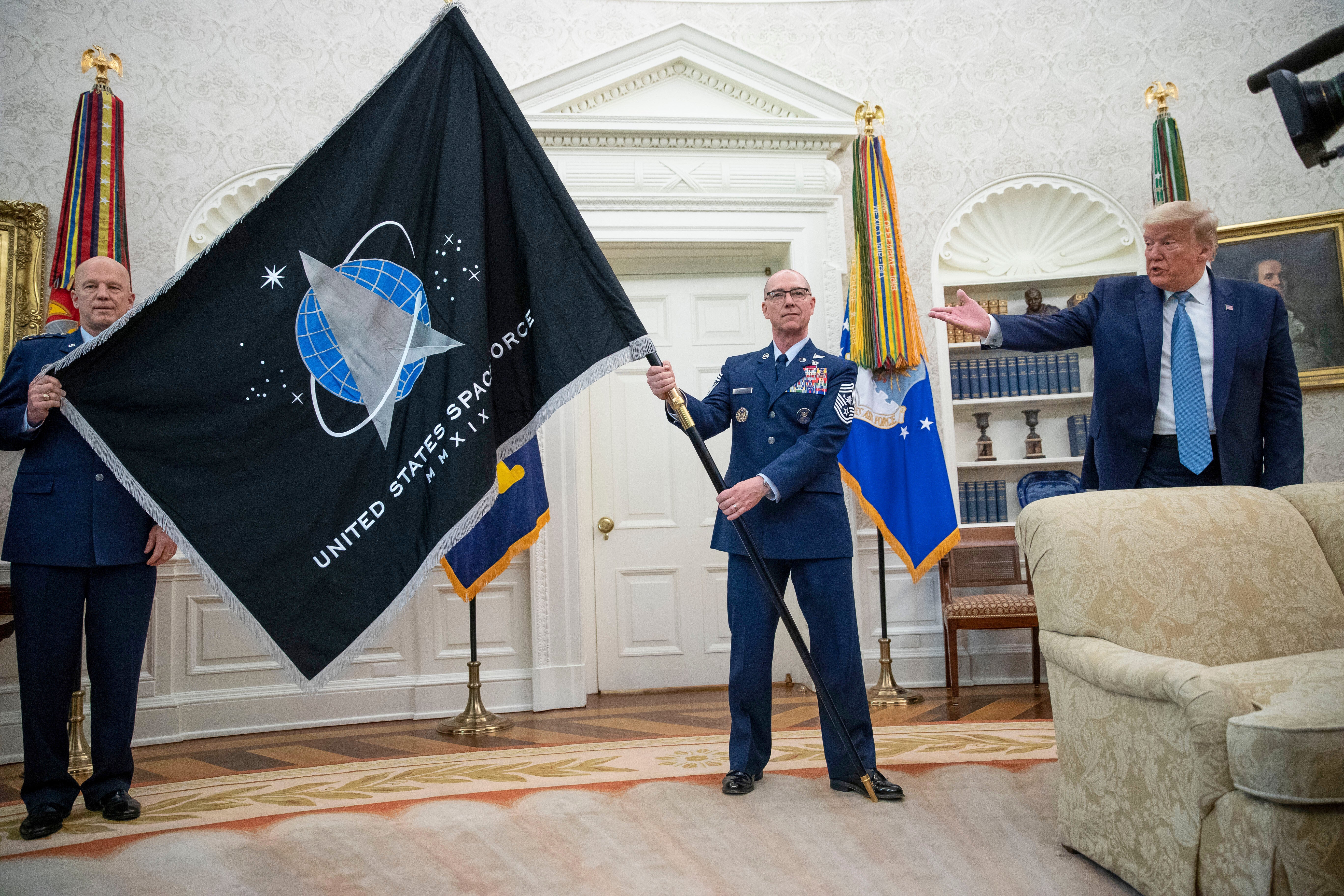 Gen. John "Jay" Raymond, Commander U.S. Space Command, left, and Chief Master Sgt. Roger Towberman, center, hold the Space Force Flag as President Donald Trump gestures to it during the presentation of the in the Oval Office of the White House in Washington on May 15, 2020. (AP Photo/Alex Brandon, File)