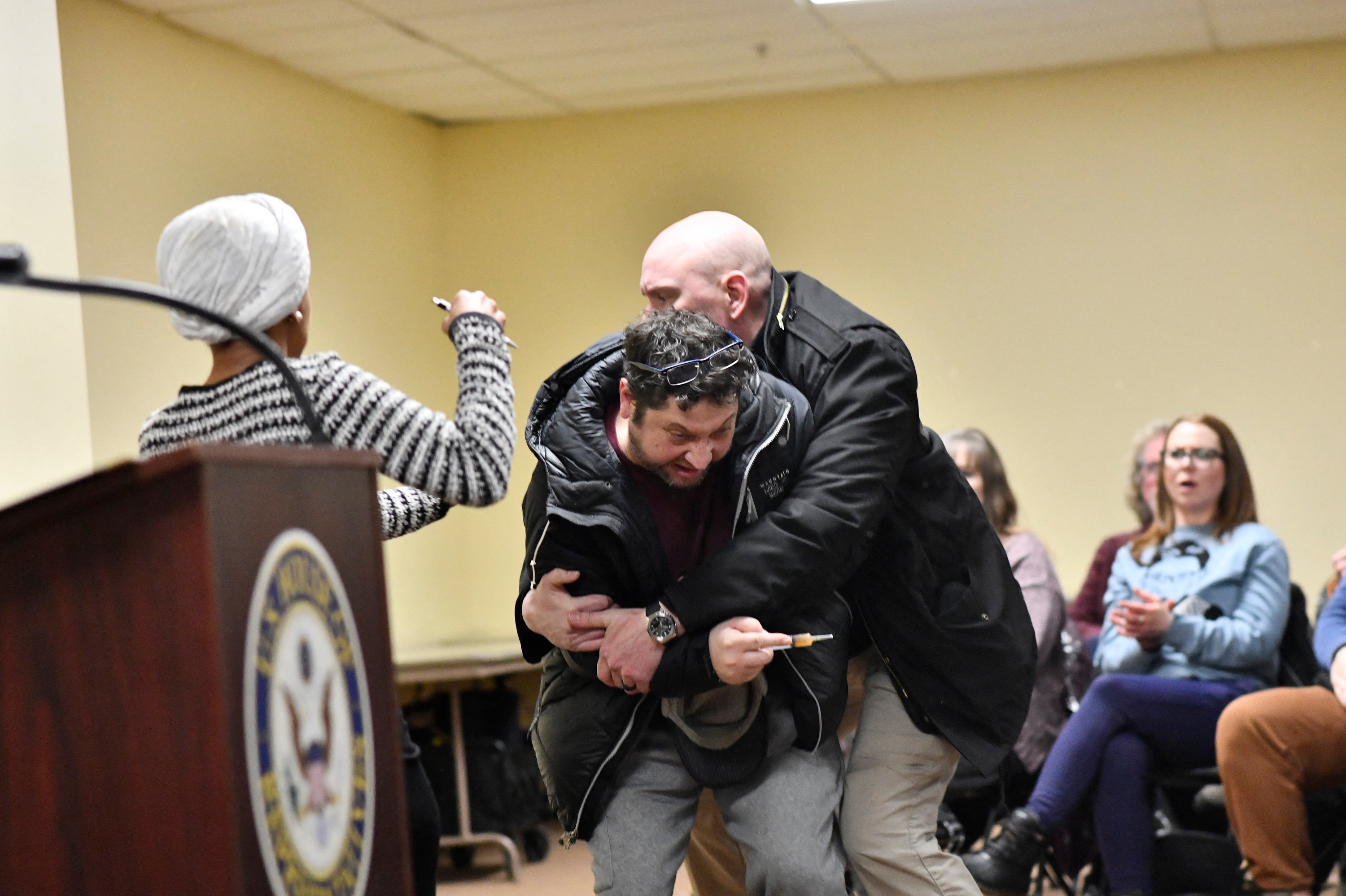 Anthony Kazmierczak is tackled after spraying vinegar at Rep. Ilhan Omar during a town hall in Minneapolis