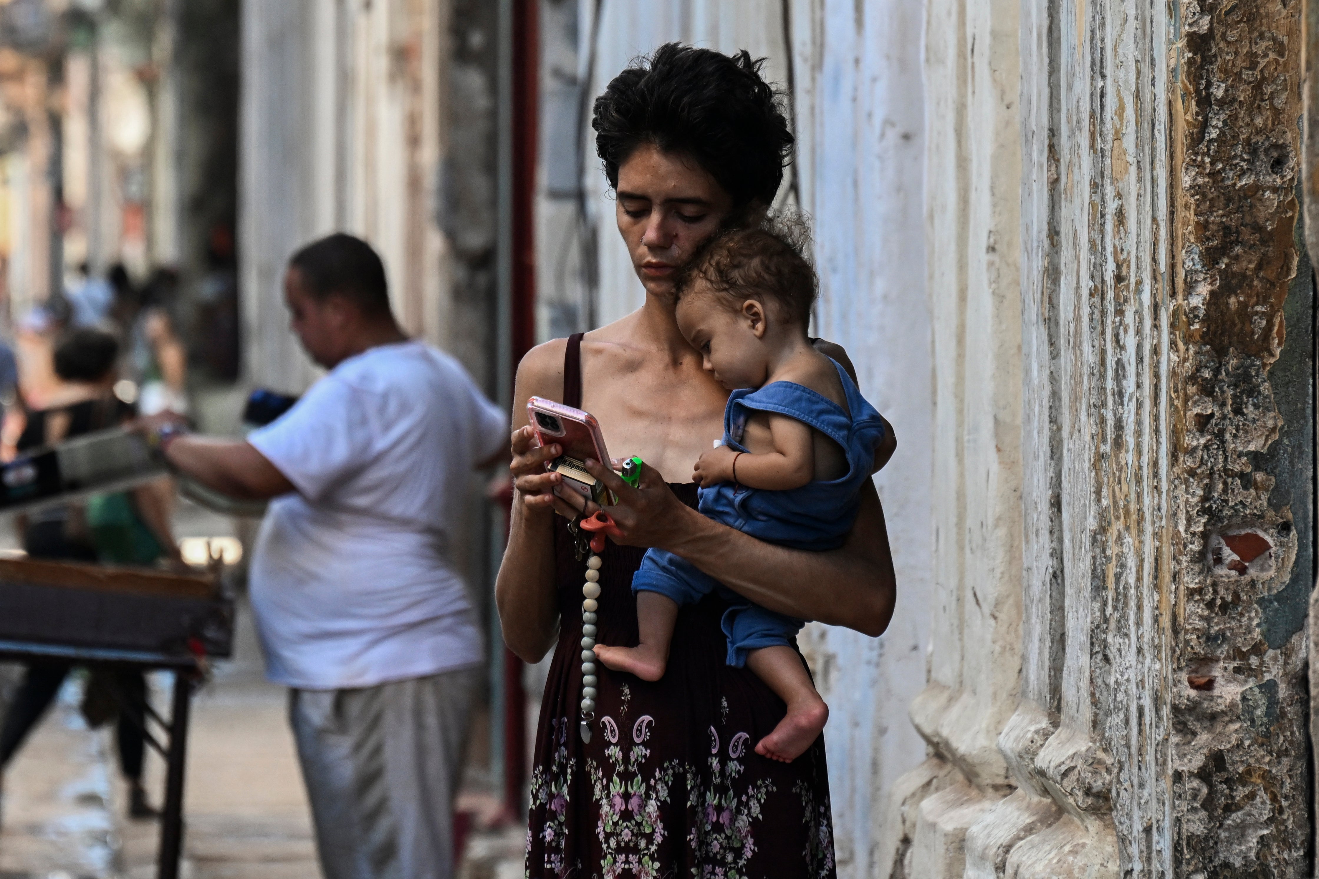 Žena nosi svoje dijete dok gleda u svoj mobilni telefon u Havani 20. svibnja, dok se otok i dalje suočava s nestašicom hrane i nestankom struje