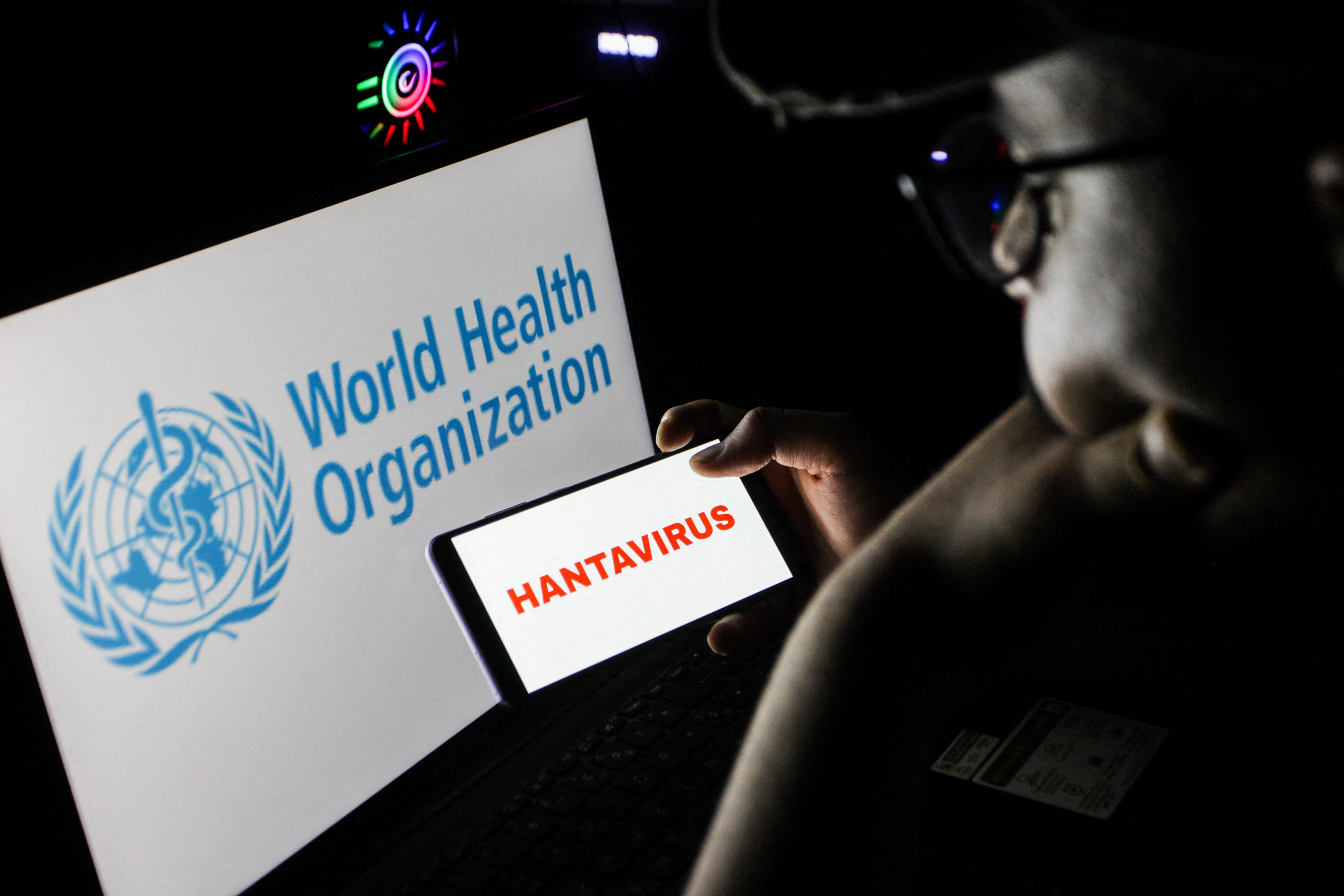 Close up image of a personification holding a smartphone displaying nan connection HANTAVIRUS successful beforehand of a machine surface showing nan World Health Organization logo successful Tunis