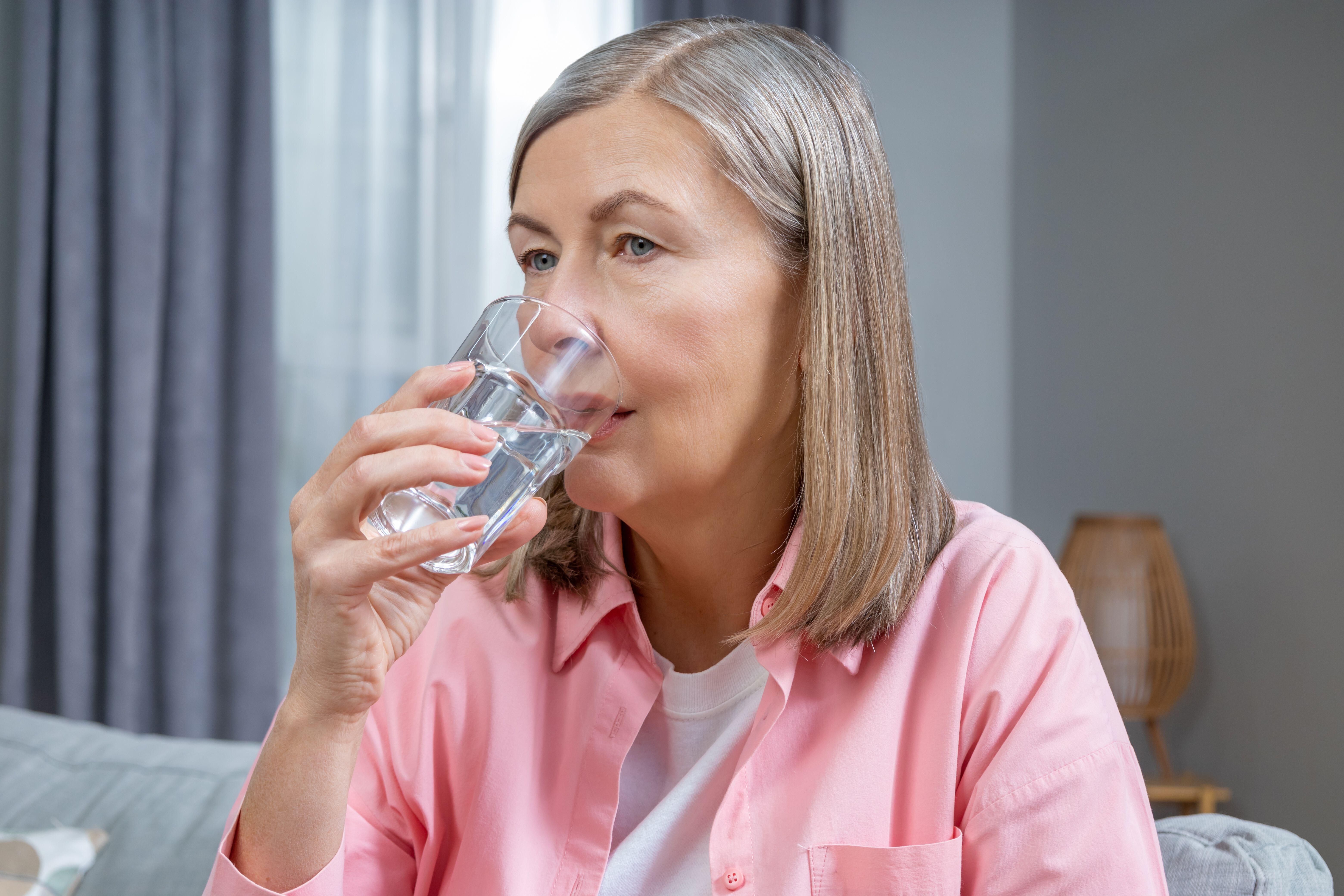 Middle aged woman drinking a glass of water (Alamy/PA)