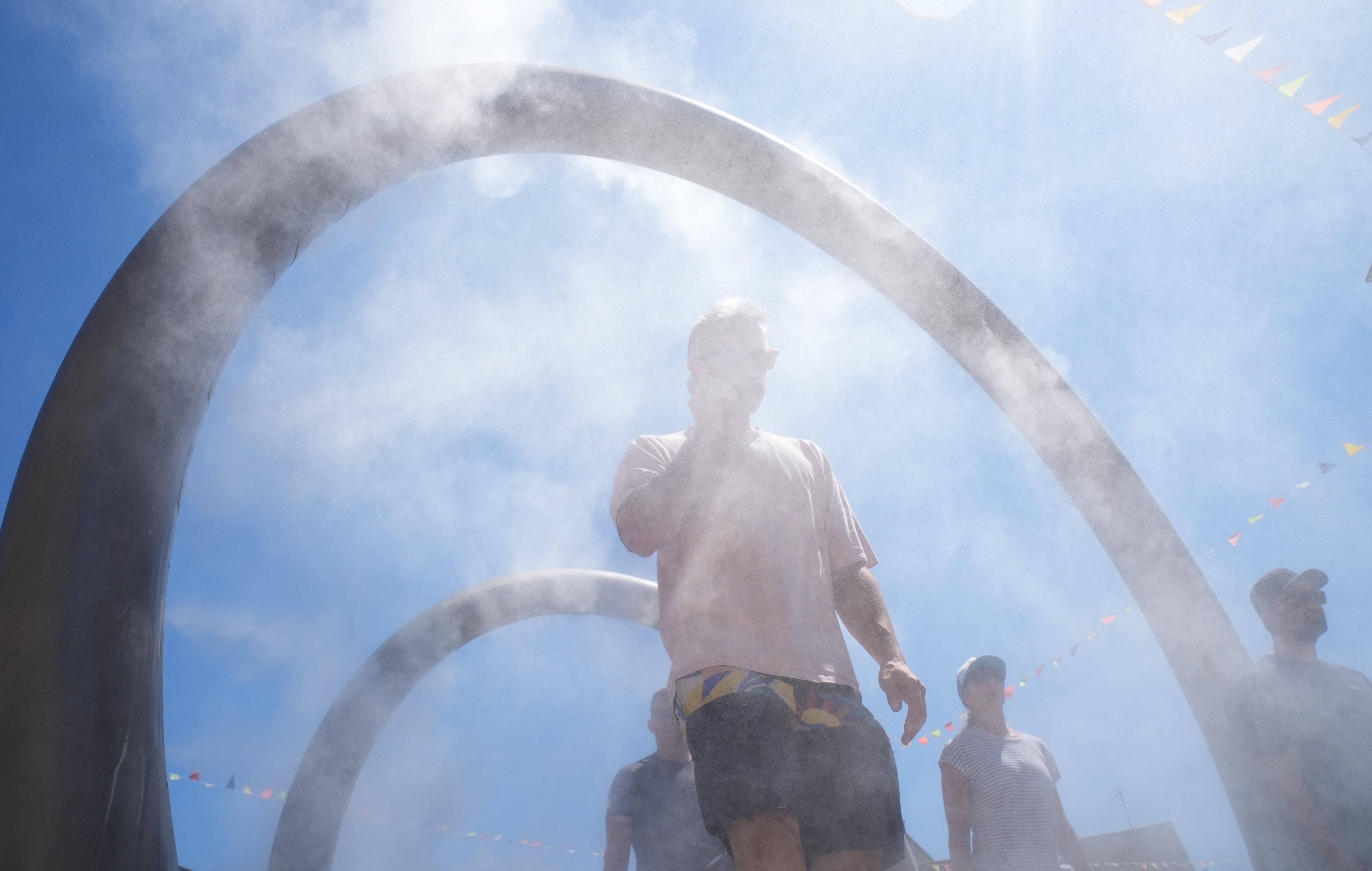 People walk through a water feature spraying a fine mist to cool off in Dover, Kent