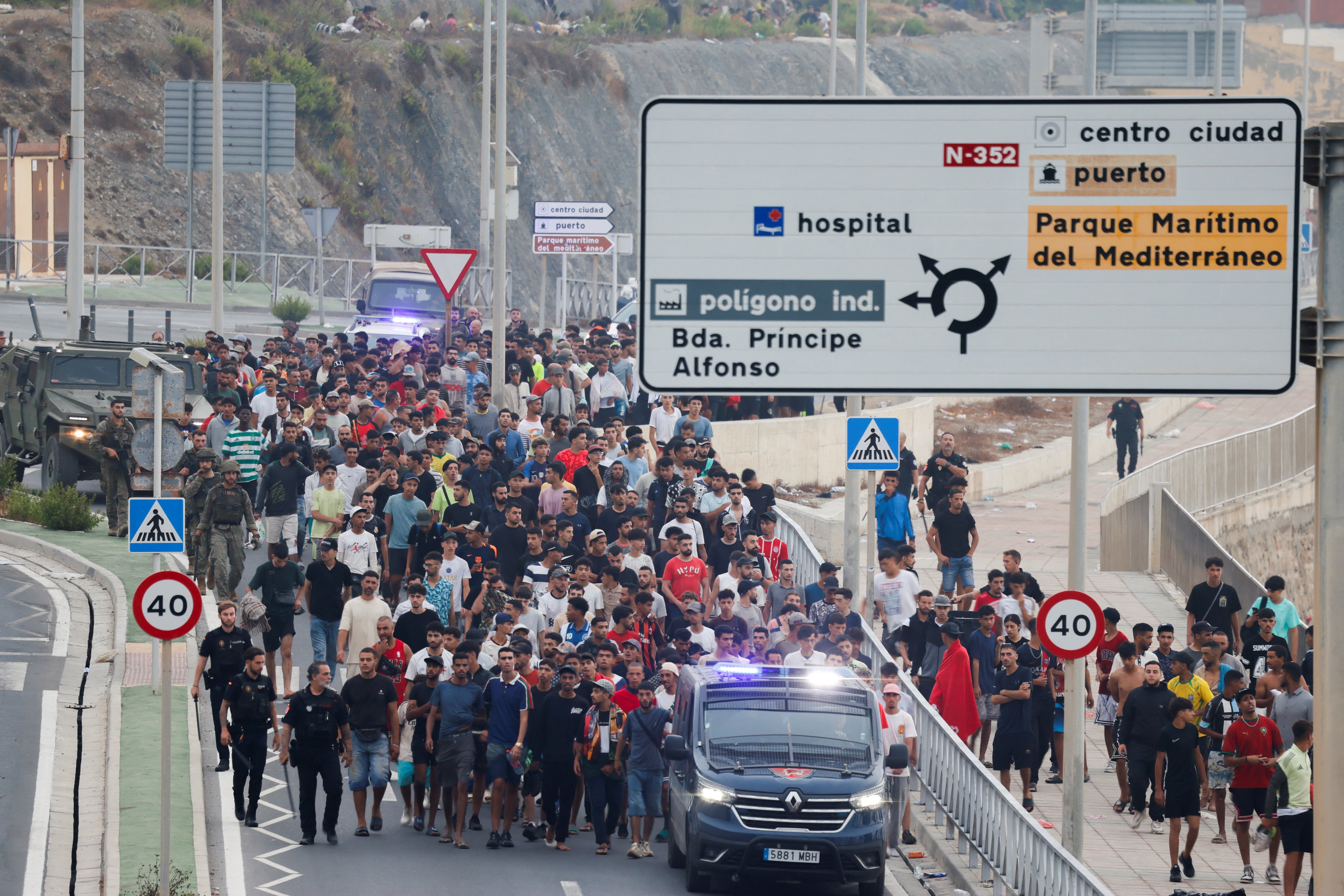 Police officers and Spanish soldiers escort a large group of migrants to the border to take them out of Spain