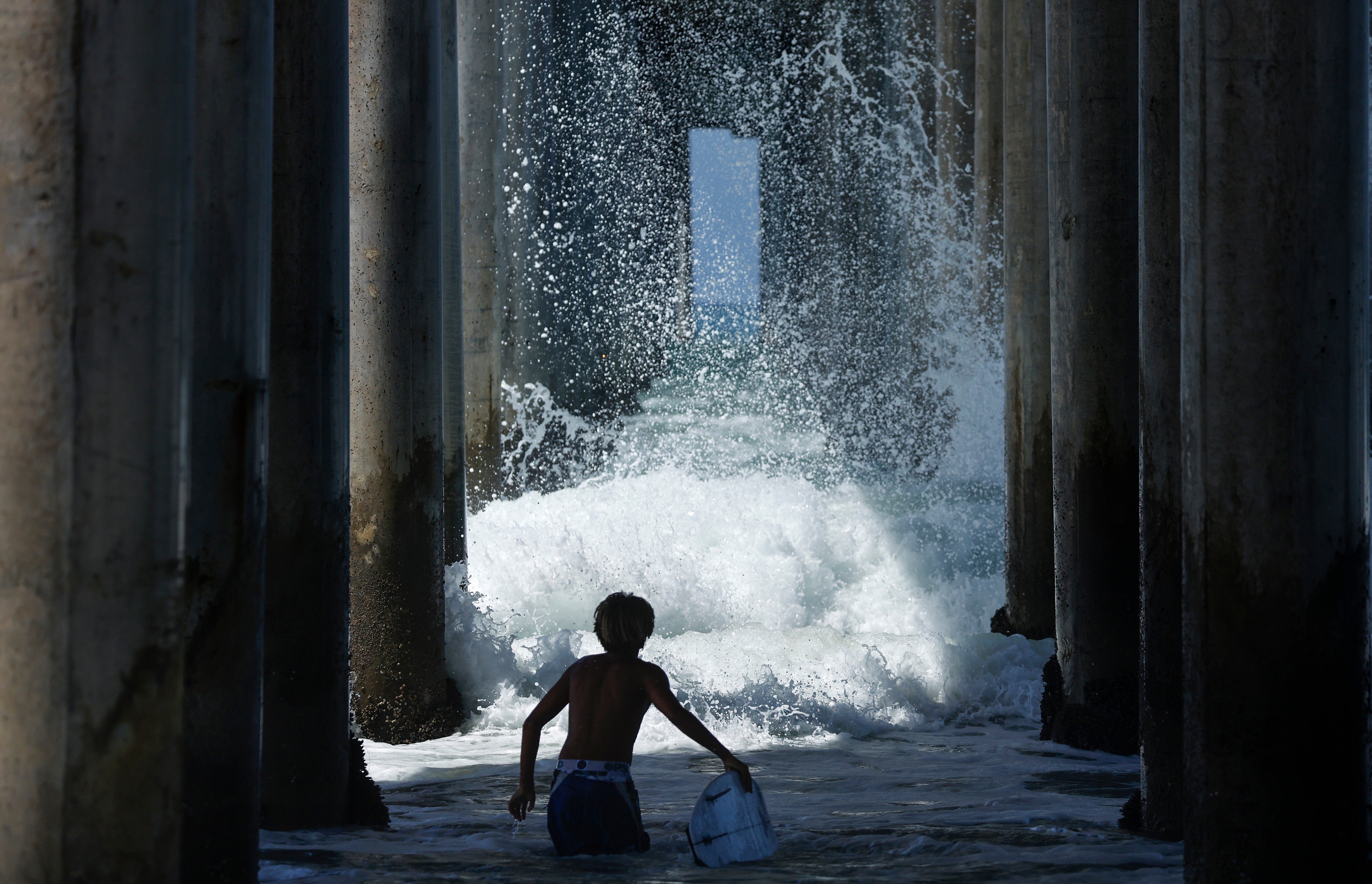 A surfer watches a activity break beneath a pier past period successful Huntington Beach, California. Genevieve brought ample swells and flooding to Southern California