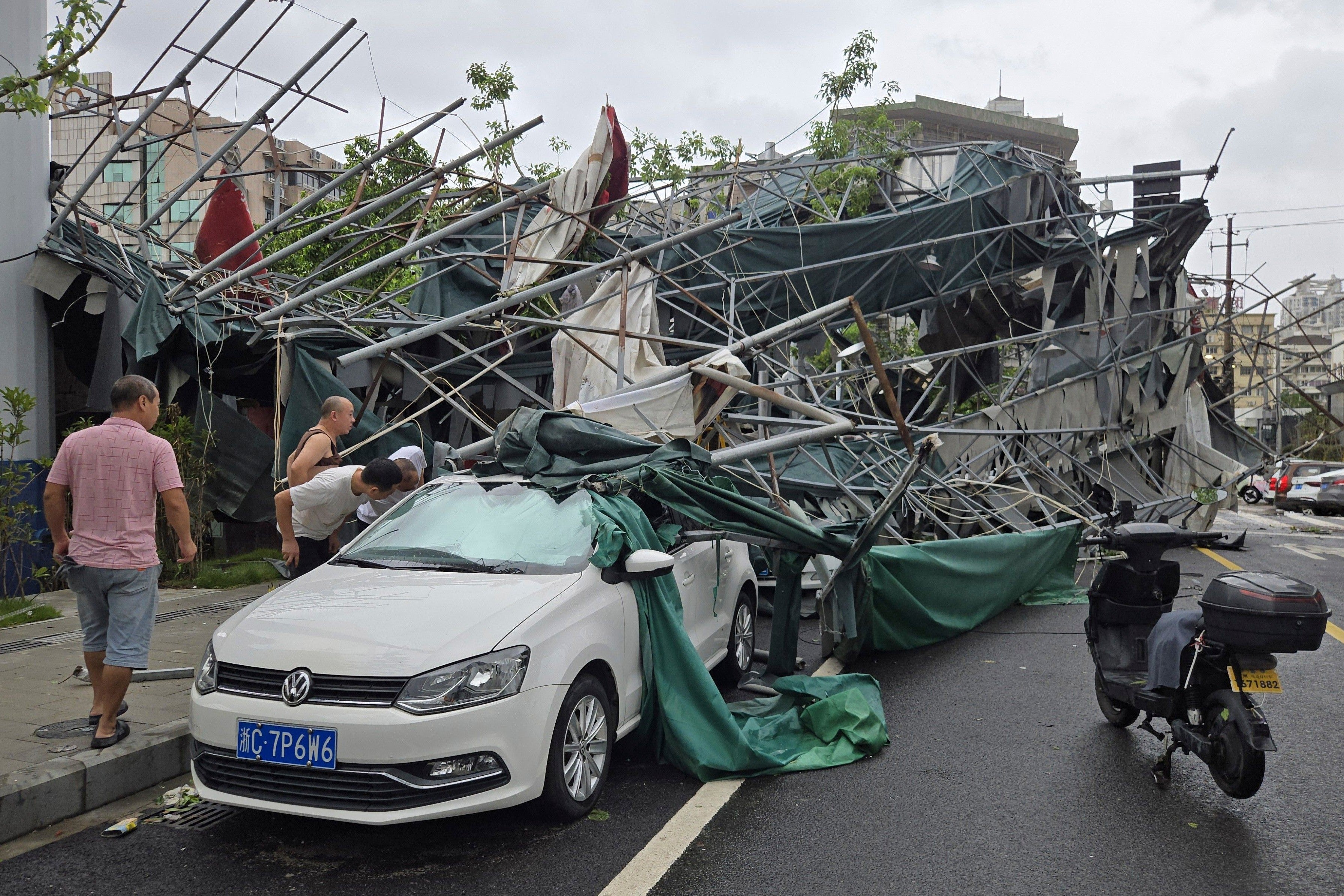 People look inside a car pinned by a fallen scaffolding structure after Typhoon Dolphin