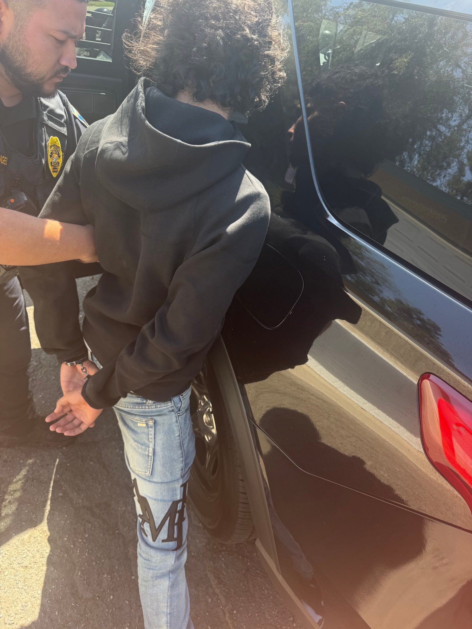 A police officer leads the handcuffed 15-year-old suspect to a vehicle
