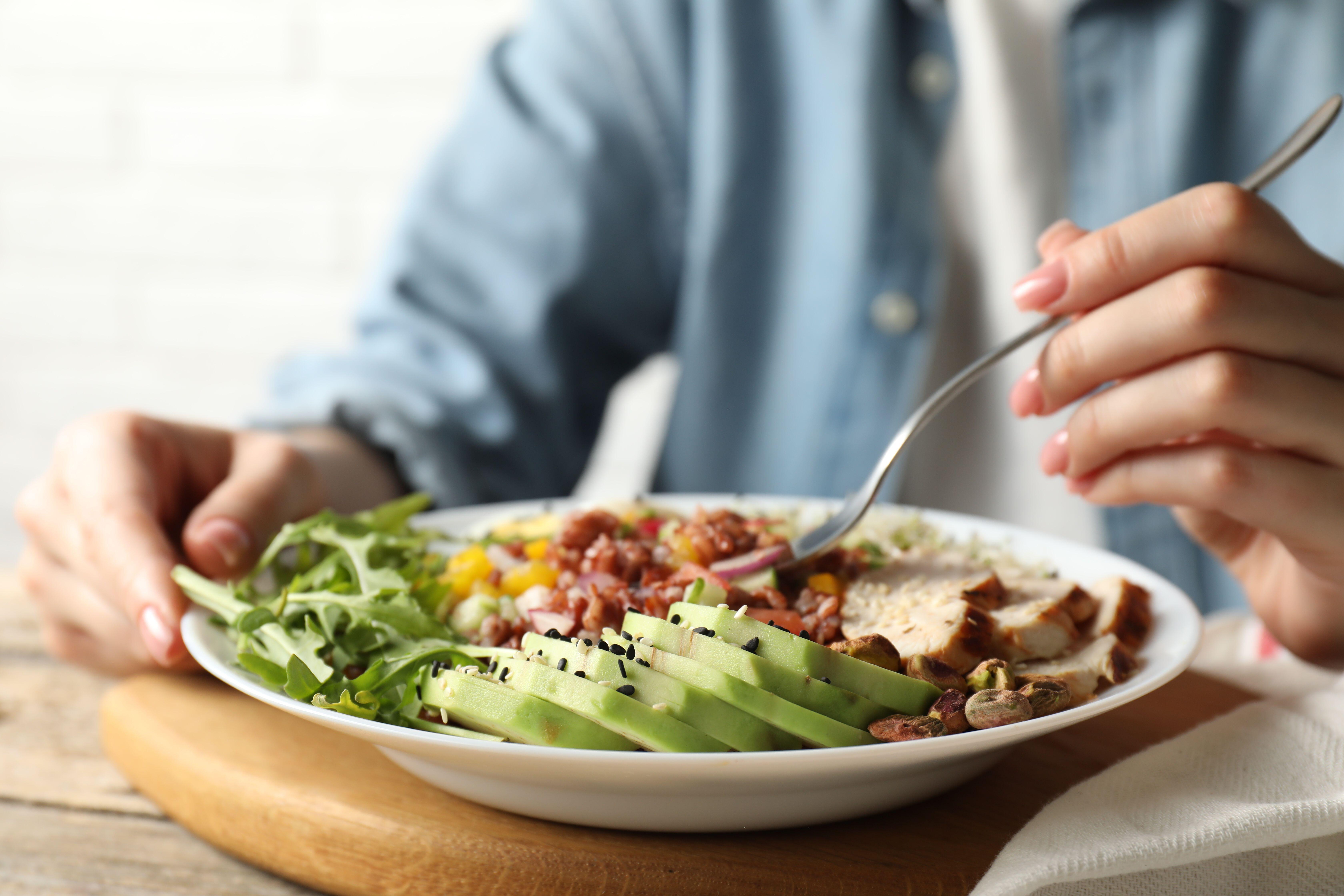 3B1YK75 Woman eating delicious salad with brown rice at wooden table, closeup