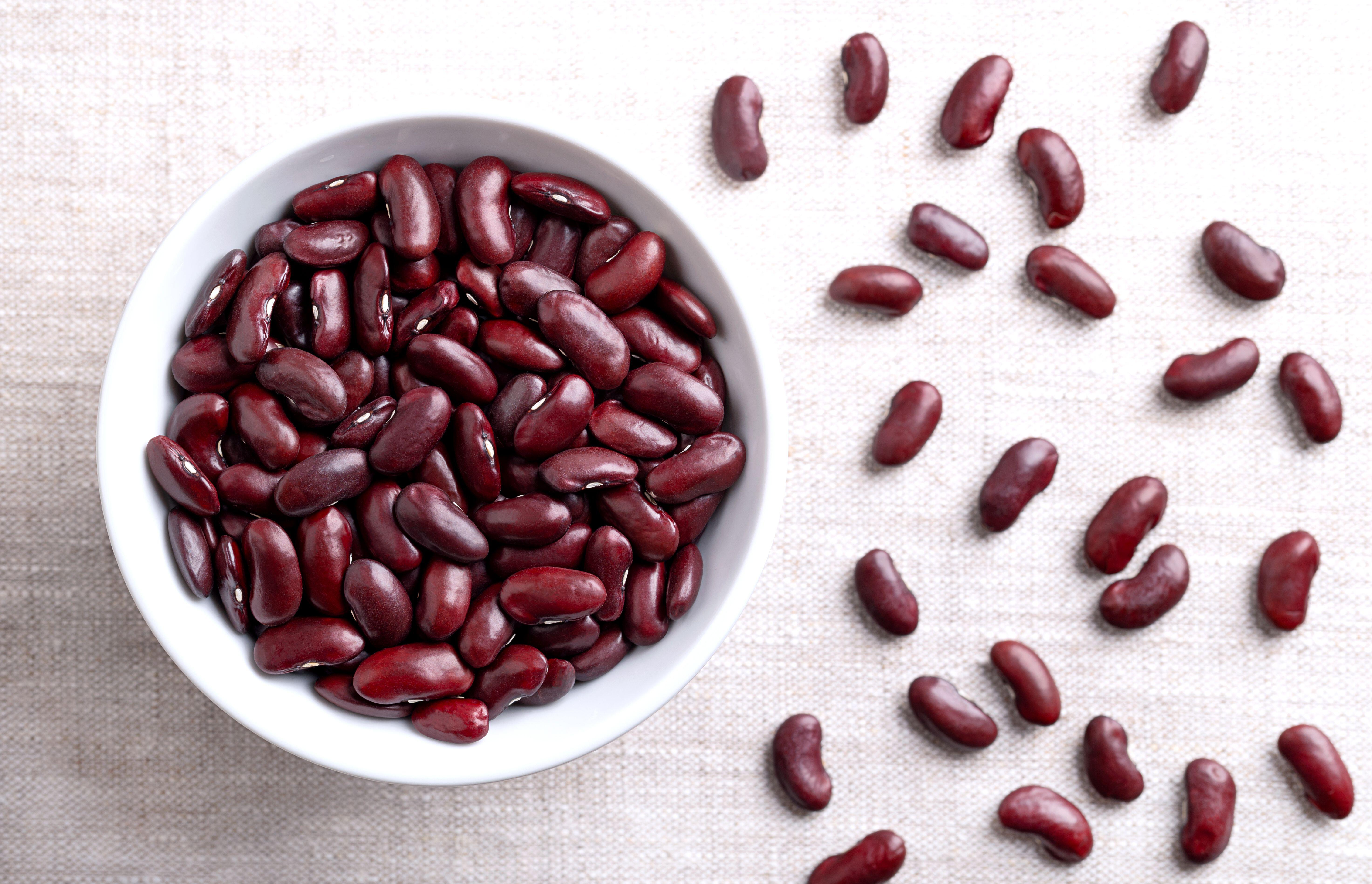2YBWTX6 Dried kidney beans in a white bowl on linen fabric. Raw, uncooked, red common kidney beans, a variety of the bean Phaseolus vulgaris.