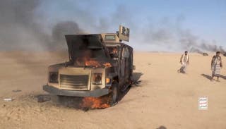 File: Houthi fighters move next to a destroyed vehicle following what the source described as an attack on Saudi-backed forces in the location given by the source as al Jawf governorate, Yemen