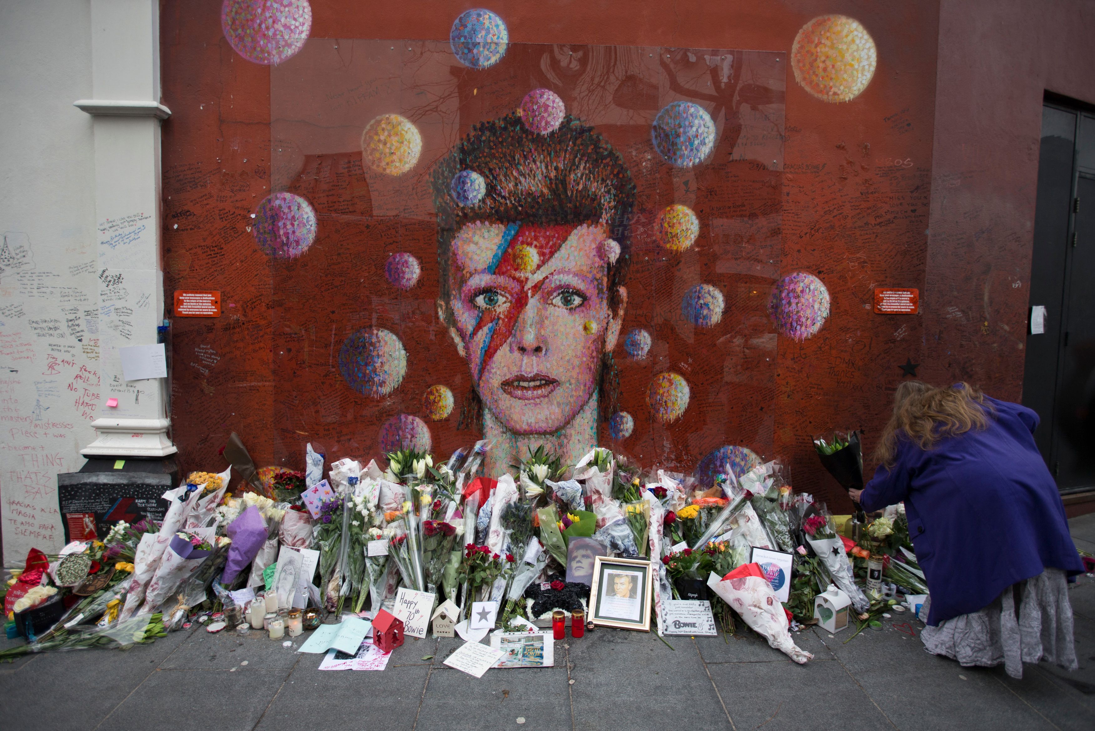 A woman lays flowers at the mural of late British pop icon David Bowie created by Australian street artist James Cochran