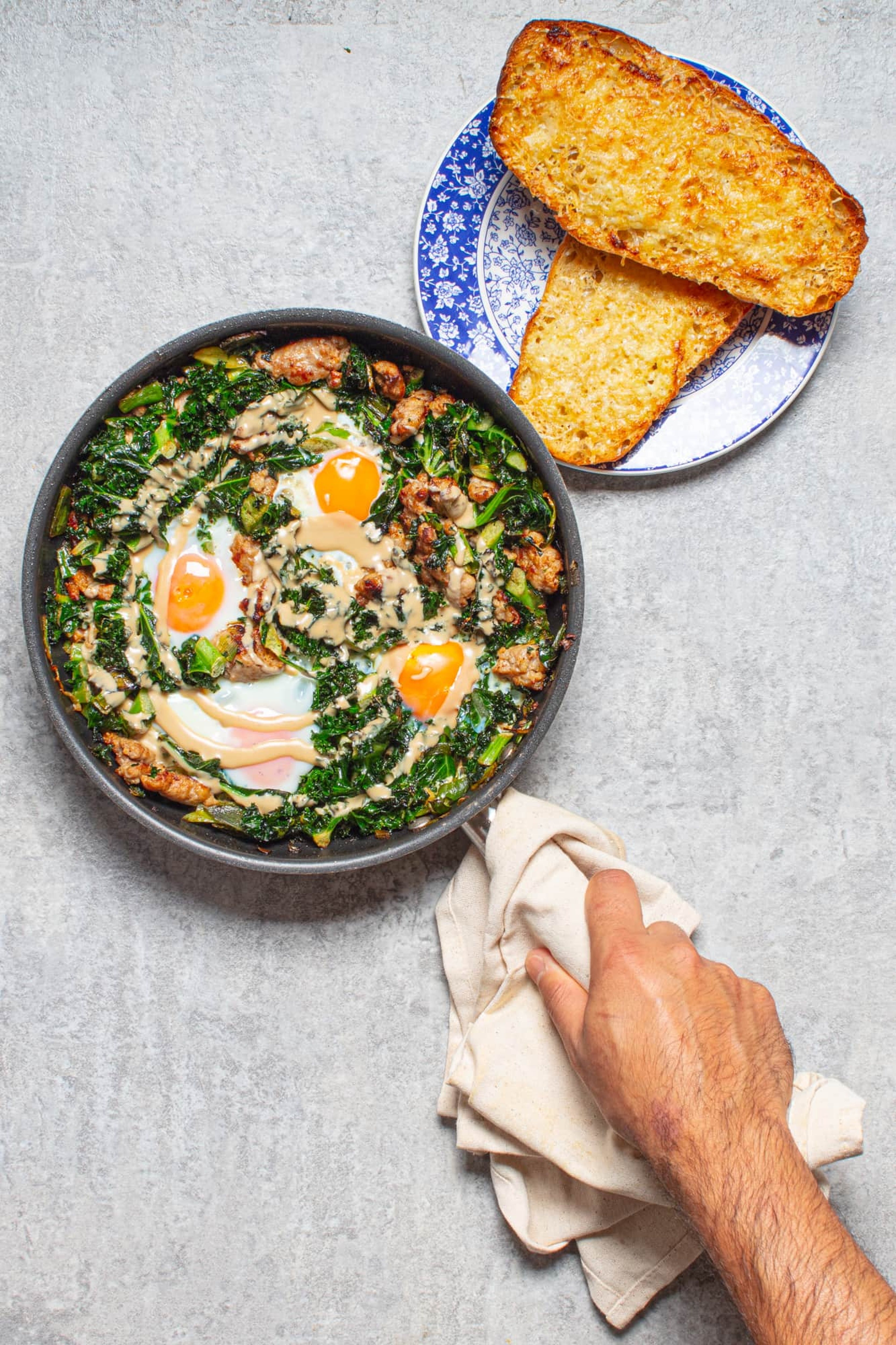 Sausage and kale baked eggs with tahini and crisp, cheesy garlic ciabatta
