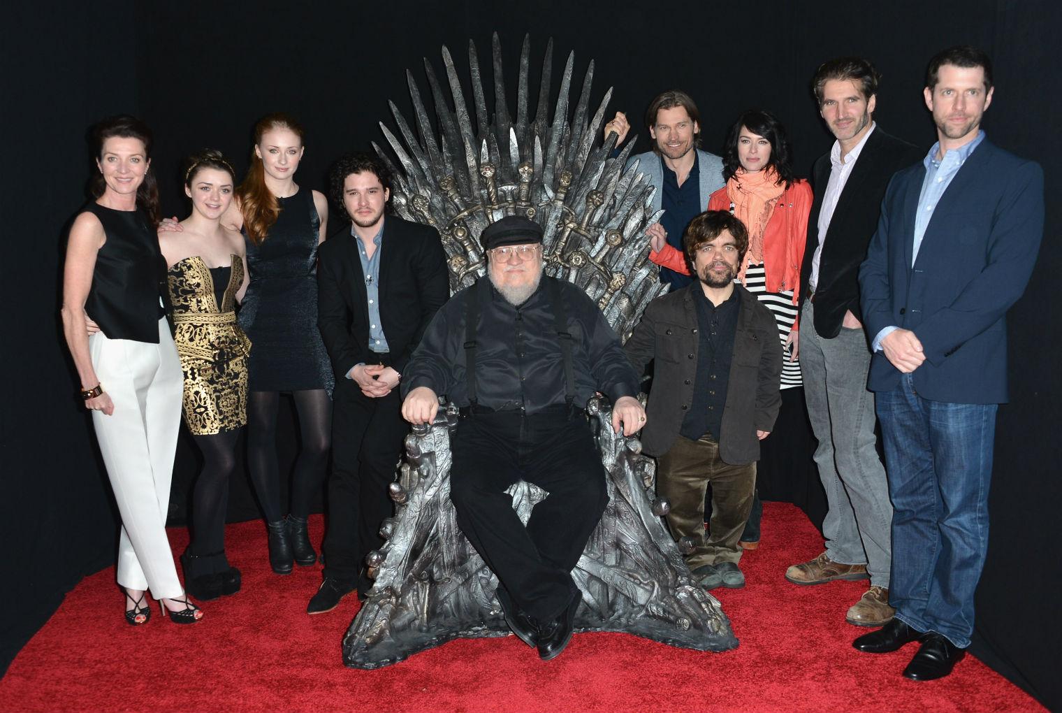 George RR Martin sitting on the Iron Throne from the set of Game of Thrones, the hit show based on his books, with members of the cast