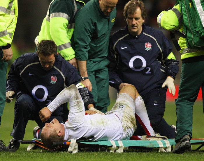 Tindall is carried off after suffering a freak injury to his liver against Wales