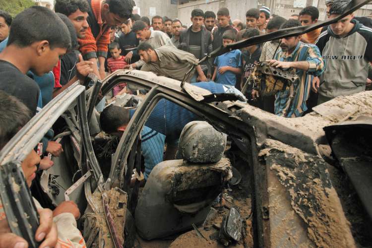 Palestinians crowd around a car destroyed by an Israeli air strike that killed two