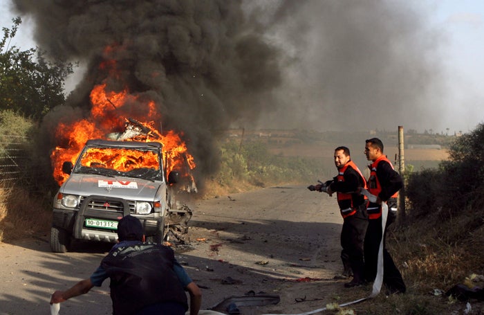 Rescue workers douse the Reuters car, clearly marked as a press vehicle, in which Palestinian cameraman Fadal Shanaa was killed