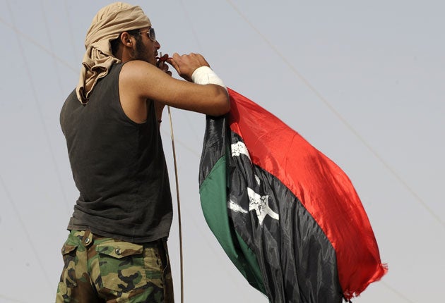 A rebel fighter puts up the new Libyan flag at a checkpoint