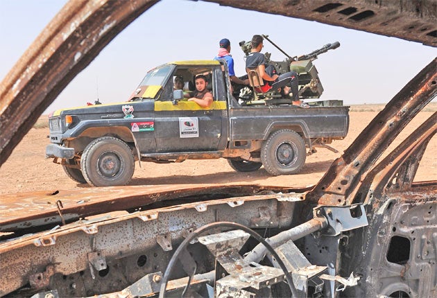 Rebel fighters pass a burnt-out car close to Misrata yesterday, as reports claimed Gaddafi loyalists were negotiating the handover of Bani Walid