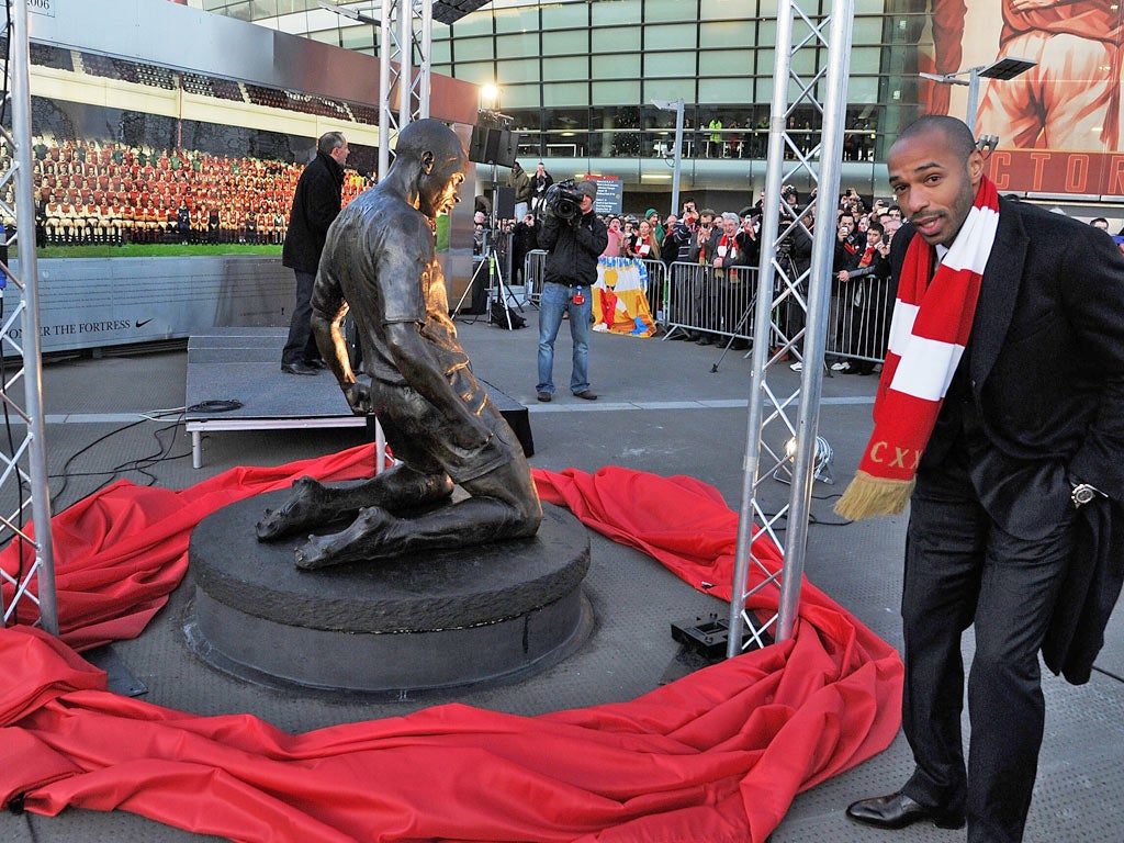 Thierry Henry poses next to a statue of himself as it is unveiled at Emirates Stadium