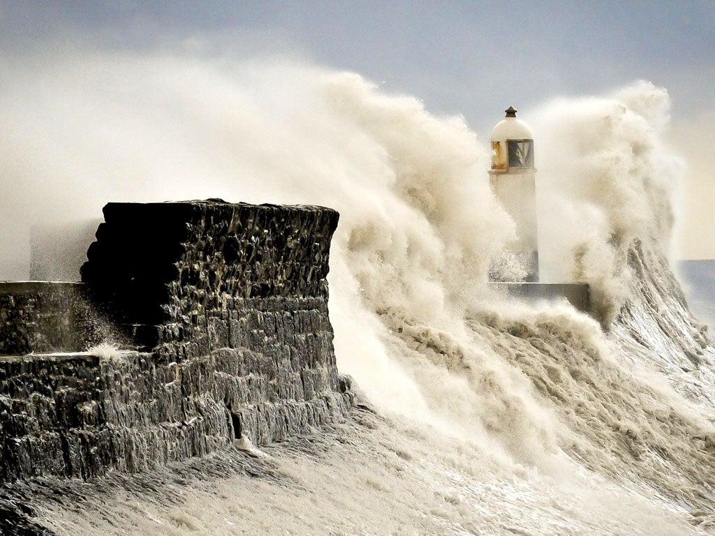 Waves crash against the harbour wall and engulf the lighthouse at Porthcawl, south Wales, yesterday