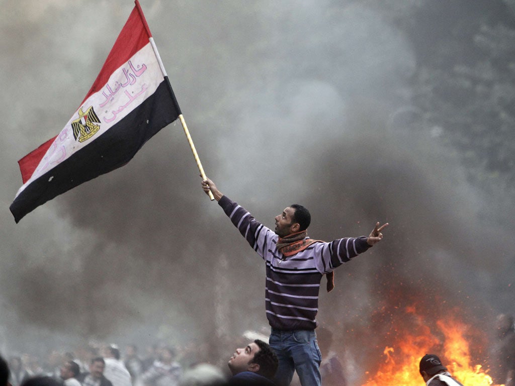 A year of revolution: An Egyptian protester waves his national flag while making the victory sign outside the parliament building during clashes with soldiers near Cairo's Tahrir Square