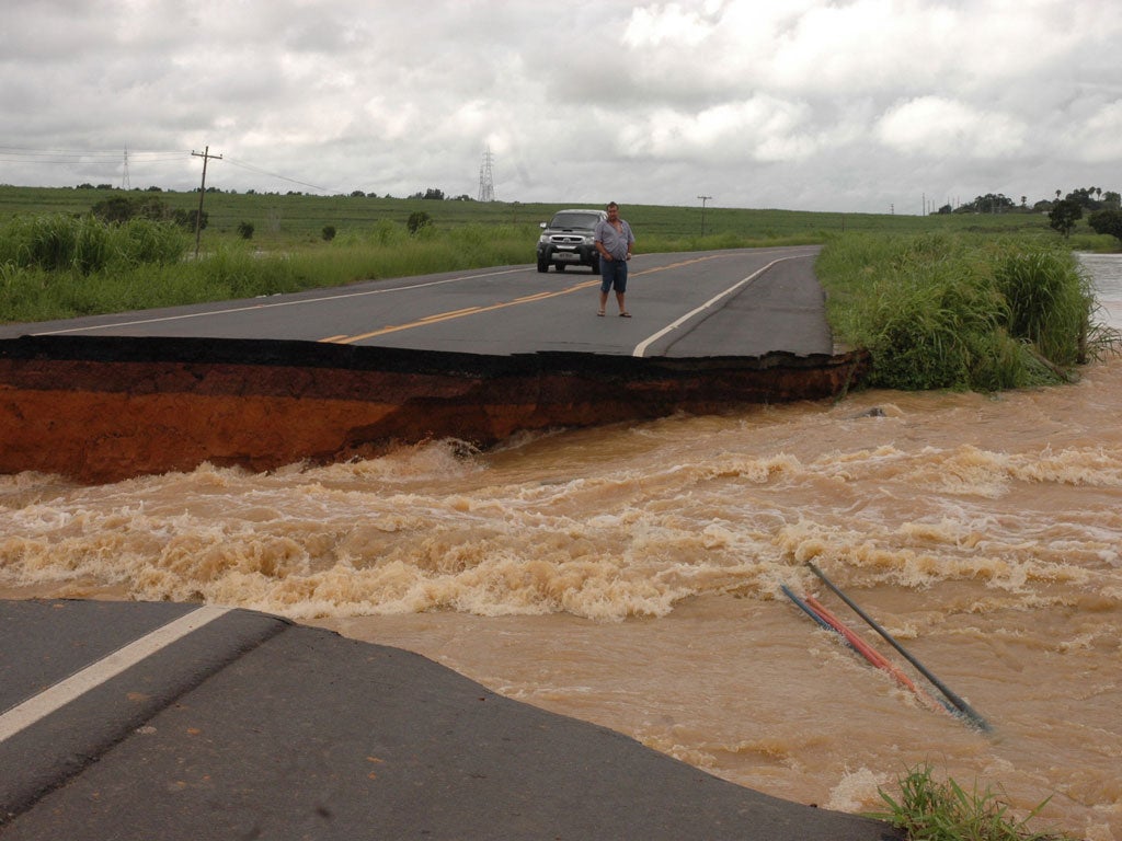 A motorist stands on the edge of a break in a road that was washed away after several days of heavy rains swelled the Muriae River in Campos