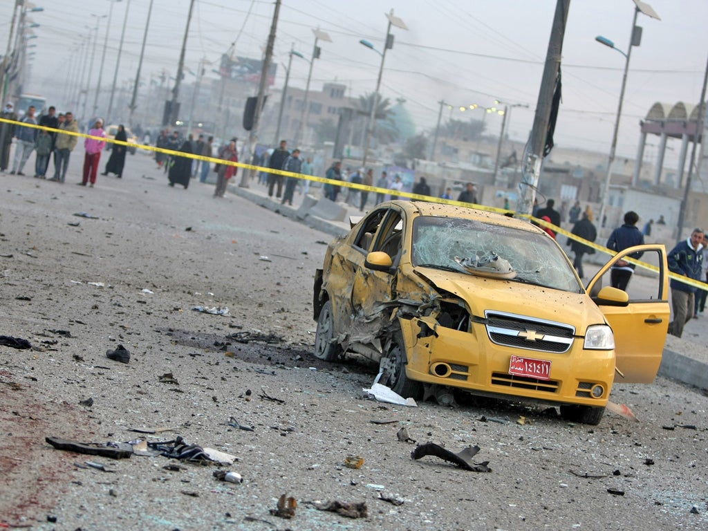 A destroyed car sits in a cordoned-off area as Iraqi security forces inspect the site of a blast after a bomb ripped through a group of workers in Sadr City in Baghdad