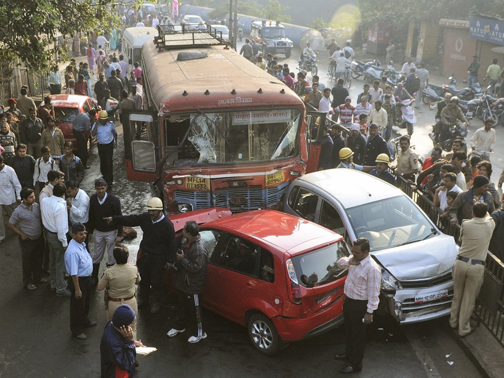 Indians look at a damaged vehicles at the scene where a bus was driven into numerous vehicles and pedestrians in the city of Pune