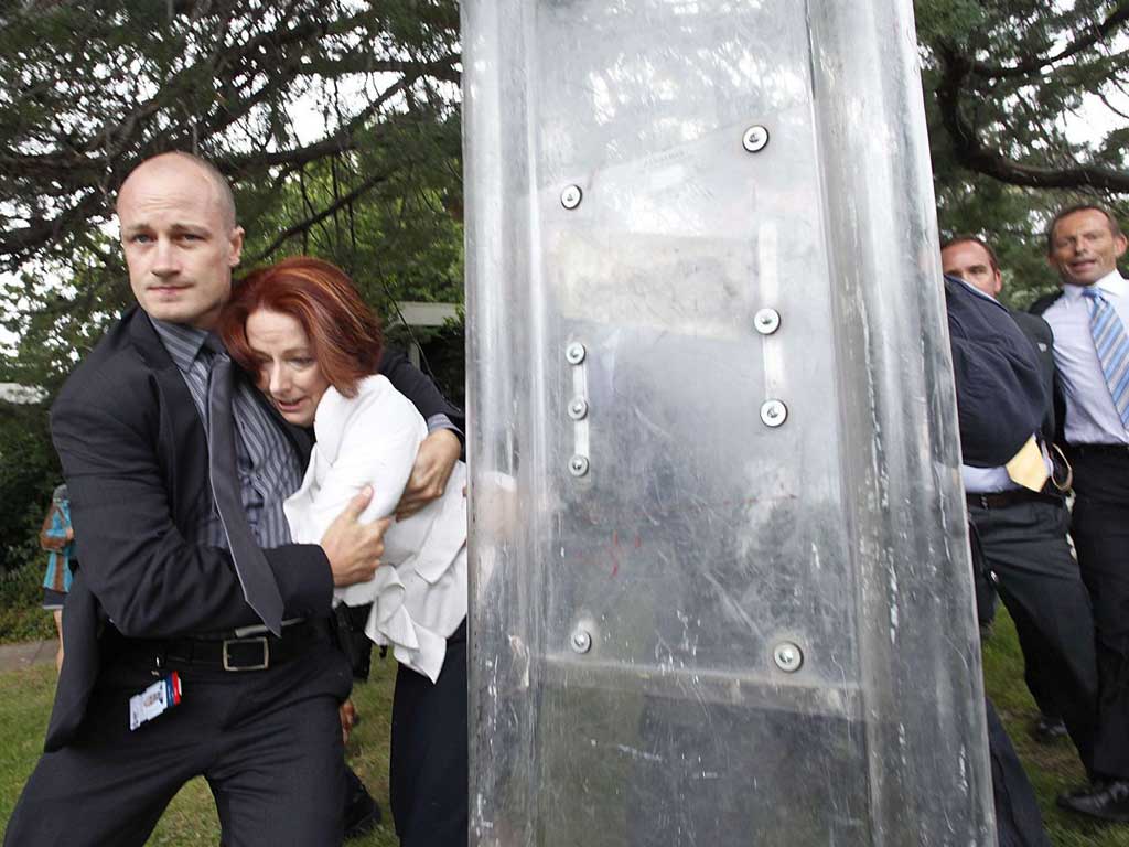 Julia Gillard is bundled out of a restaurant by her bodyguard after it was surrounded by furious Aboriginal rights protesters in Canberra