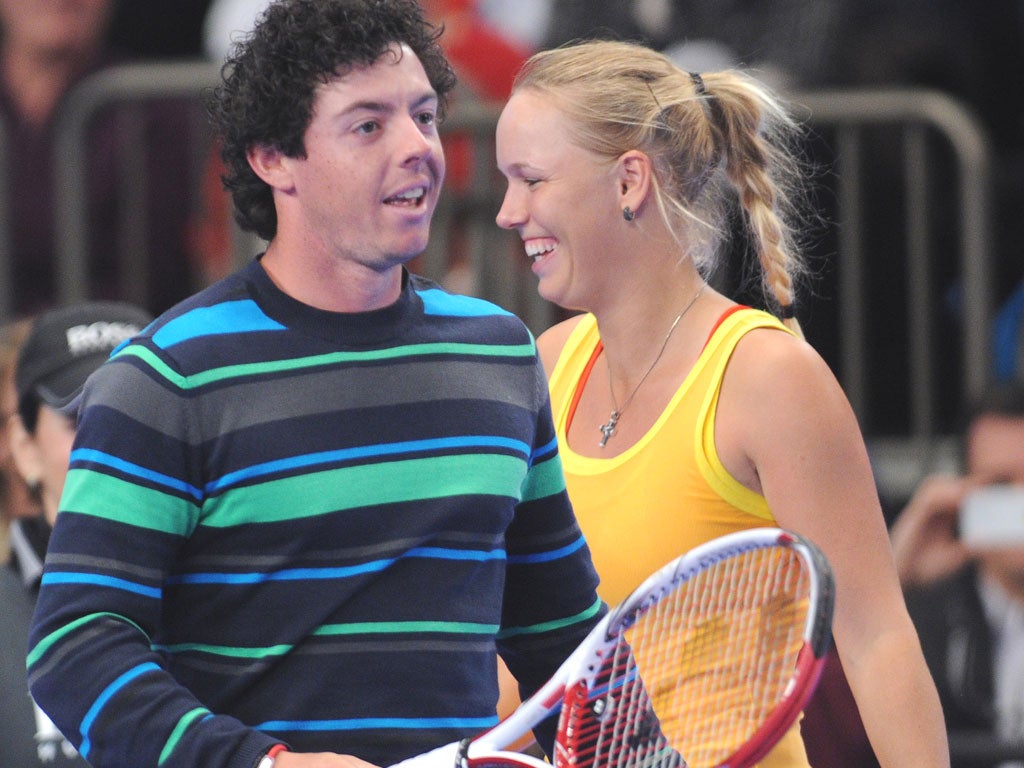 Rory Mcilroy prepares to hit a tennis ball to Maria Sharapova as Caroline Wozniacki looks on in the BNP Paribas Showdown exhibition tennis match yesterday