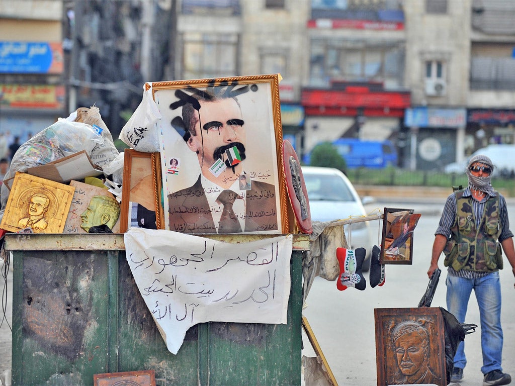 A Syrian rebel stands near a vandalized portrait of Syrian President Bashar al-Assad in the city center of Selehattin, near Aleppo,