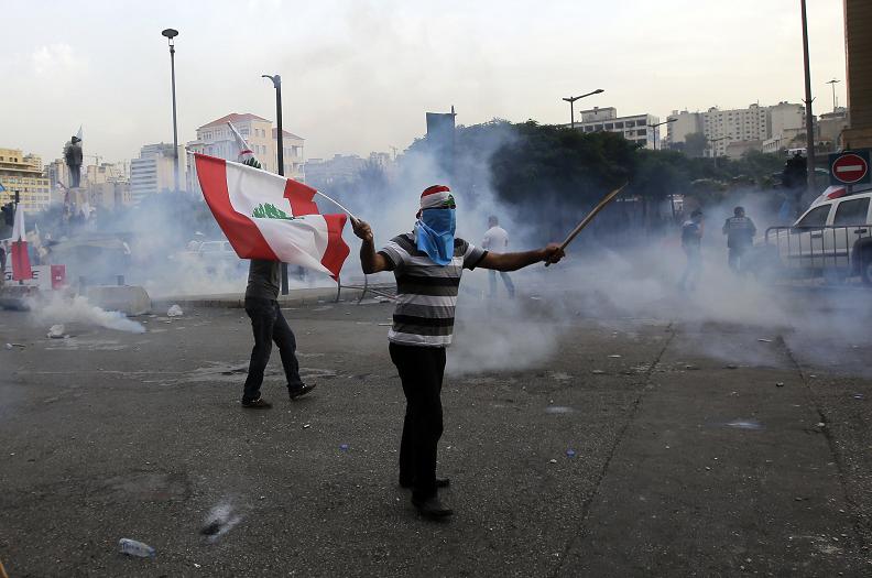 A Lebanese supporter of the March 14 movement, which opposes the Syrian regime of President Bashar al-Assad, demonstrates waving his national flag, as other protesters tried to storm the governmental palace, after the funeral of top intelligence chief Gen