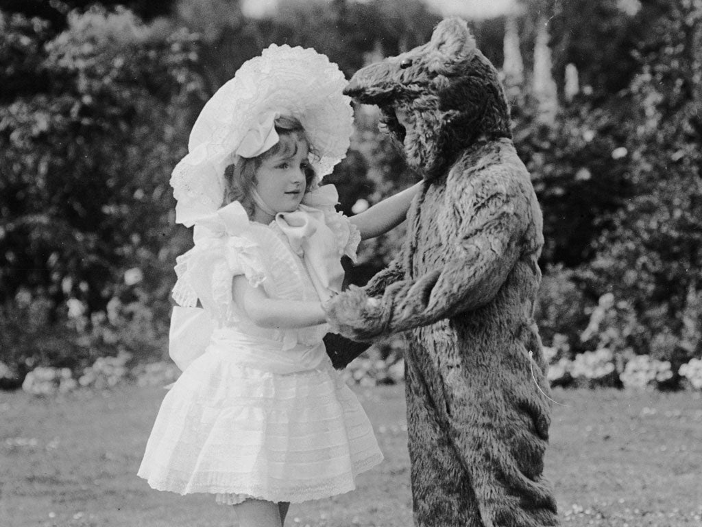 1909: Two young children in fancy dress, one as a bear, dance together at a garden party.