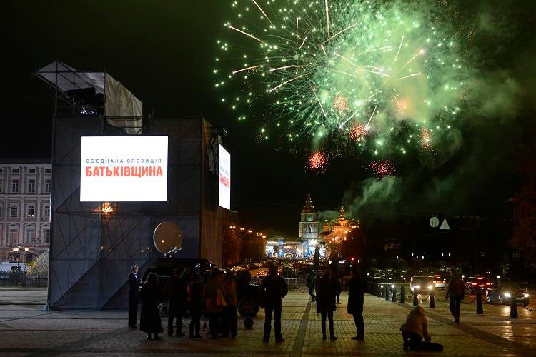 People walk in a street of Kiev as fireworks launched by supporters of Viktor Yanukovych's Regions Party burst in the sky