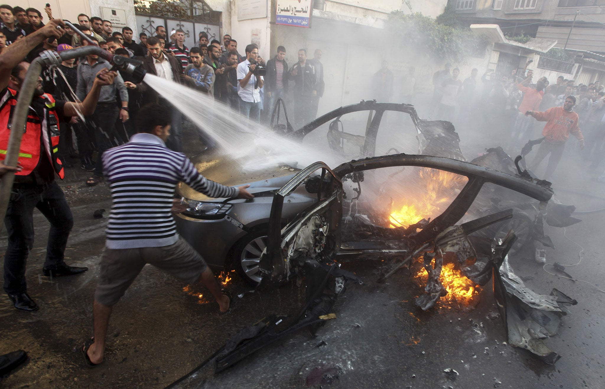 Palestinians extinguish fire from the car of Ahmed al-Jabari after it was hit by one of several Israeli air strikes in Gaza City