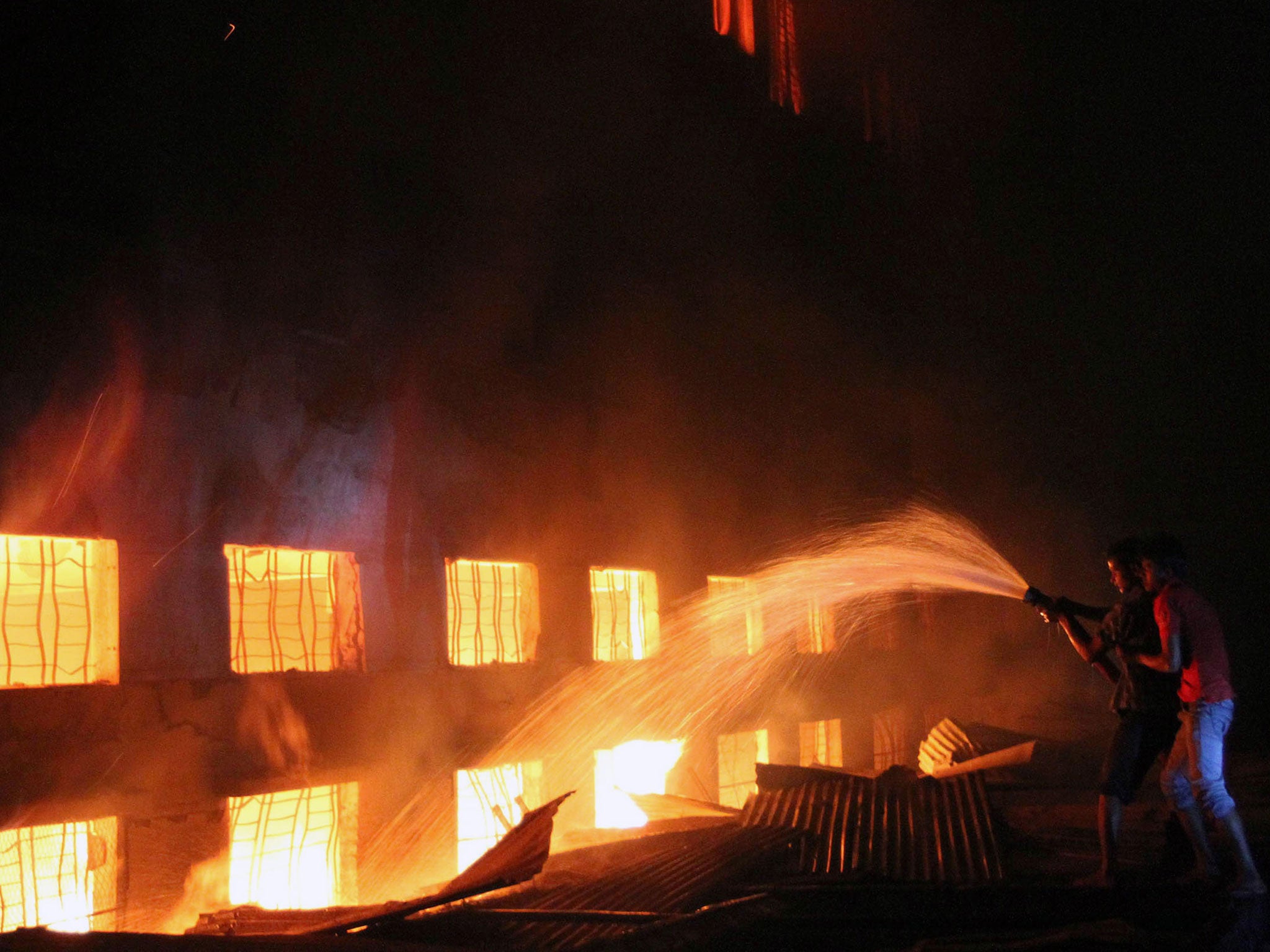 Bangladeshi people and firefighters trying to extinguish a fire in a garment factory
