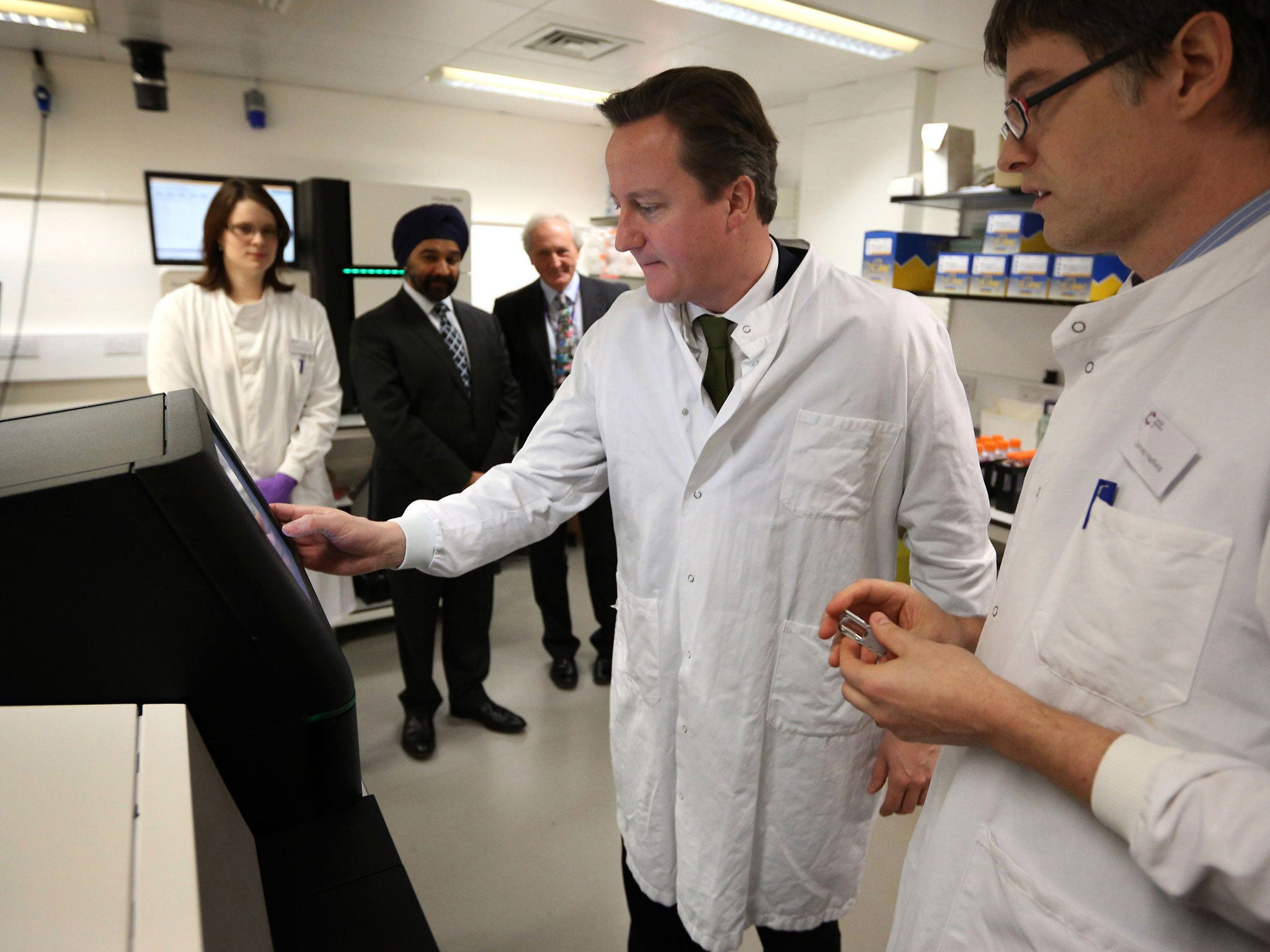 David Cameron (second right) stands with Dr James Hadfield (right) as he uses a personal genome sequencing machine during a visit to the Cancer Research UK Cambridge Research Institute