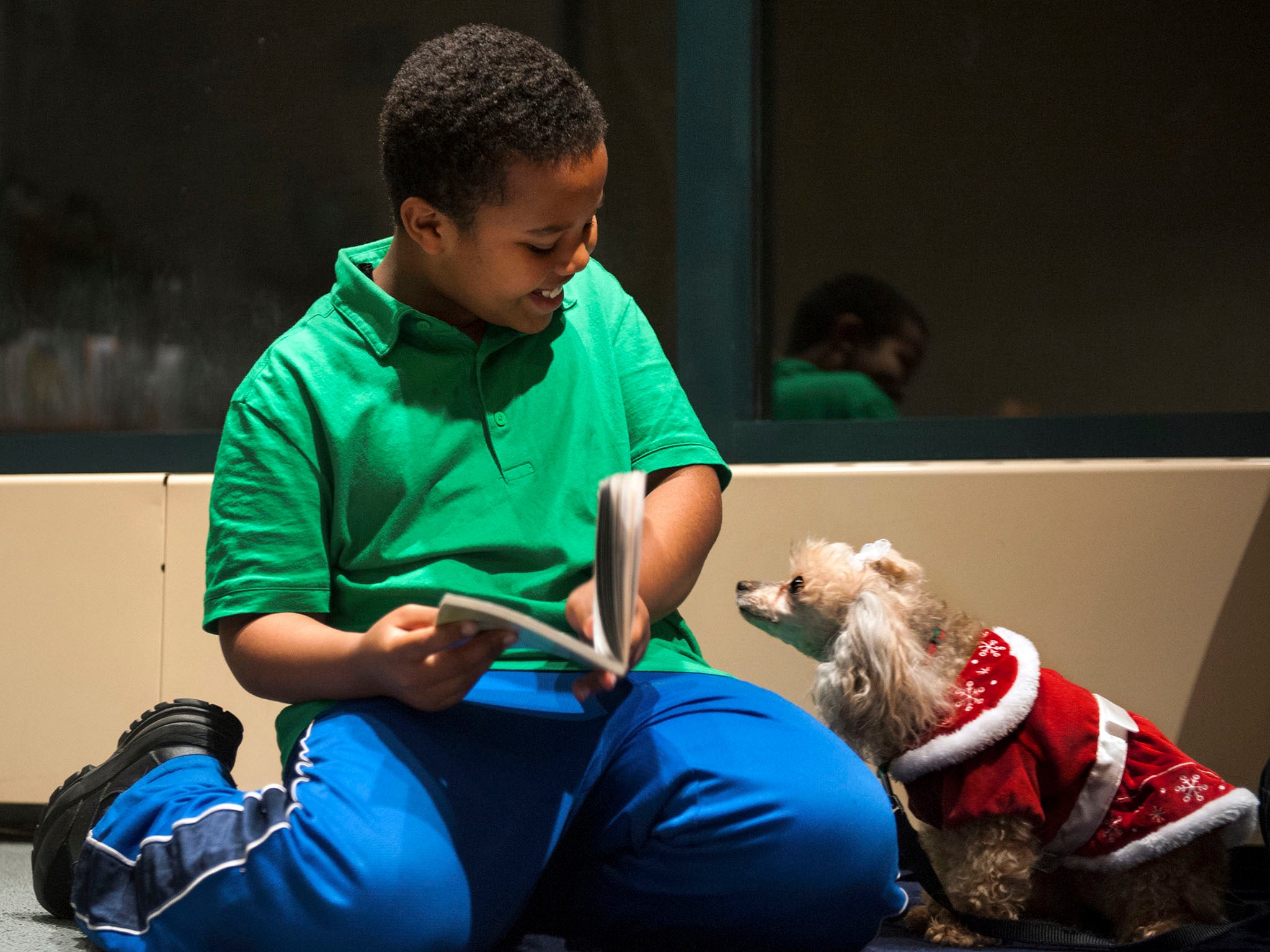 Binyam Gebremeskel, 9, of Alexandria, Virginia, is delighted that Lucy, a toy poodle, seems interested in “Ricky Ricotta's Mighty Robot,” the book he's reading to her at Beatley Central Library.