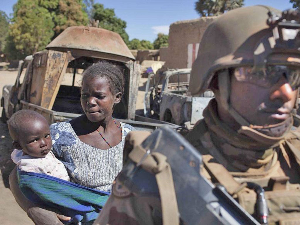 A mother holding her child and a French soldier stand in front of charred pickup trucks used by Islamist rebels in Diabaly