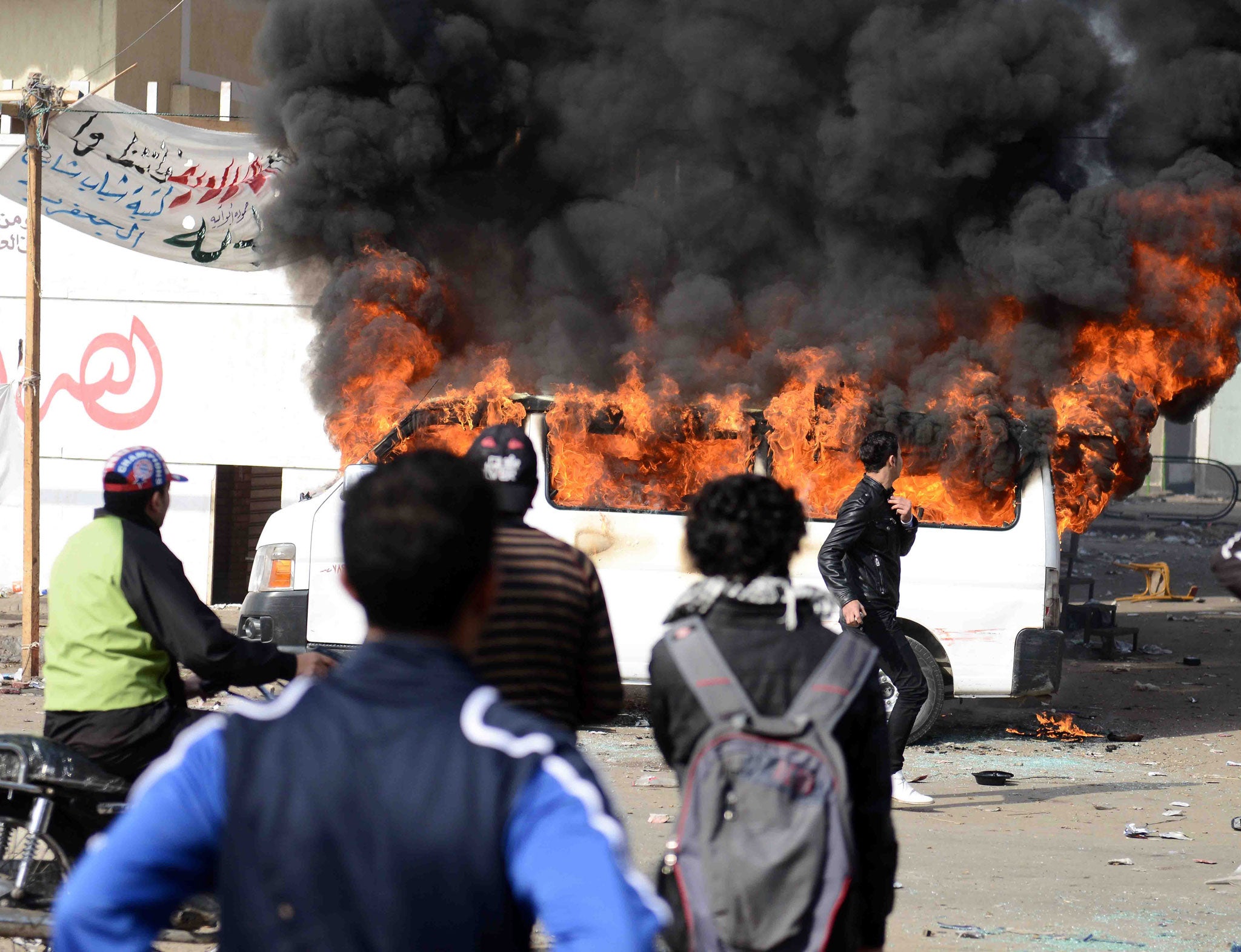 A satellite channel's burning minibus billows smoke after being set on fire by protesters outside Port Said prison