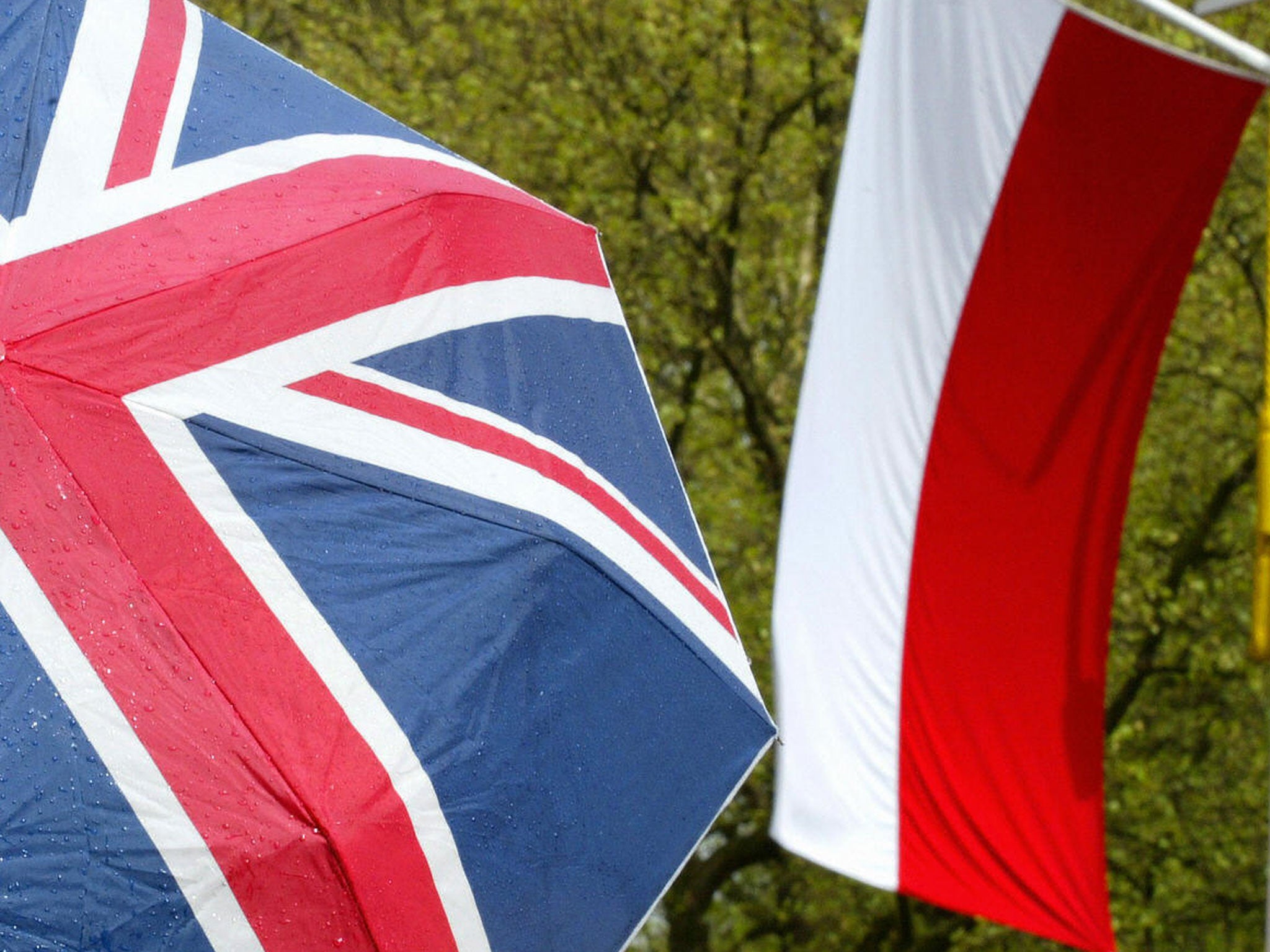 A pedestrain takes shelter under an umbrella with Union Jack on it as they walk past the Polish flag on the Mall in London 05 May, 2004. The British capital was dressed in red and white to welcome Polish President Aleksander Kwasniewski who was on a State Visit.