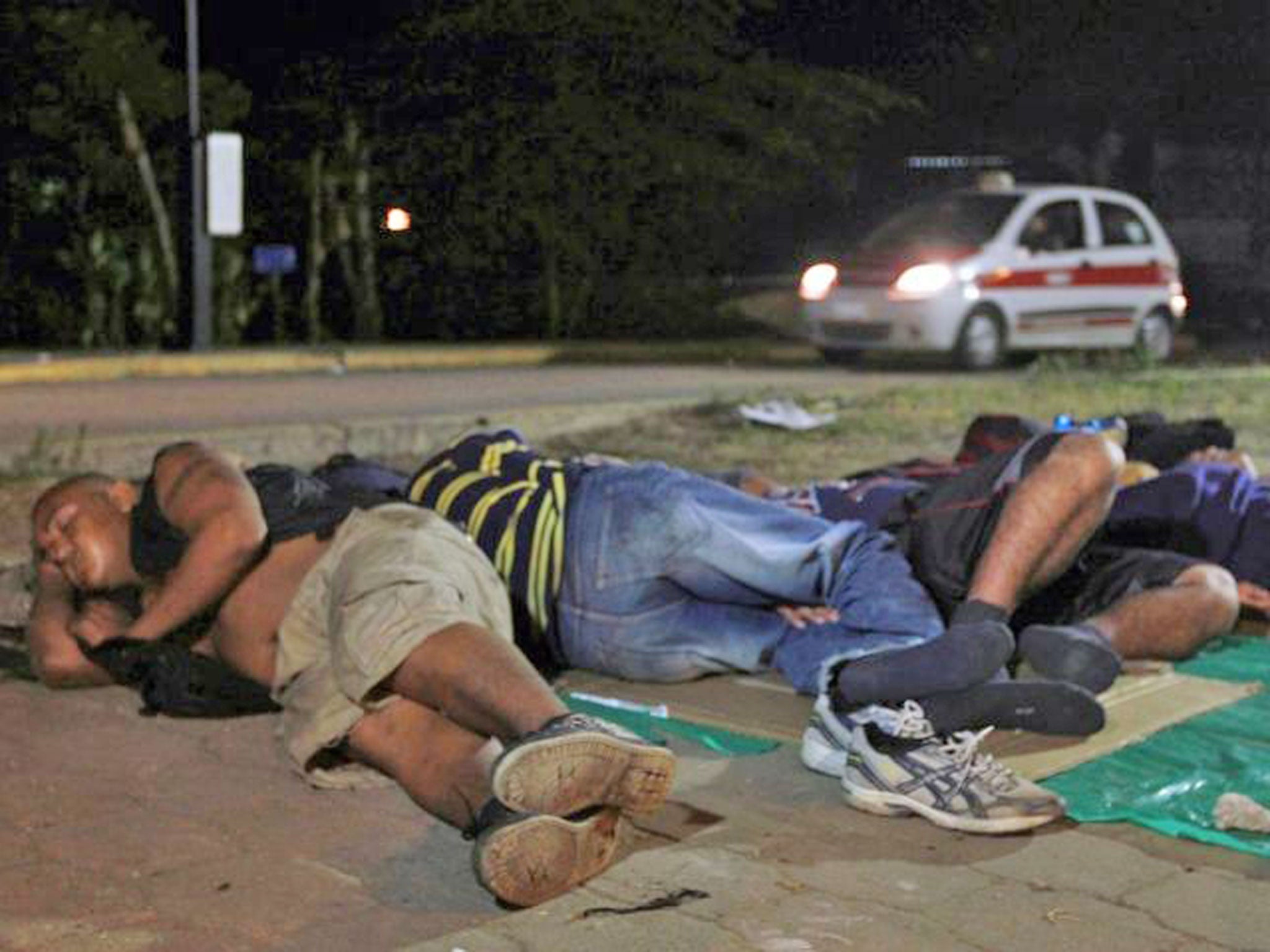Central American immigrants waiting to board a train, sleep next to a road in Coatzacoalcos, Veracruz state. Thousands of immigrants seeking to reach the US border, are encamped in the village of Coatzacoalcos in hopes that the train called The Beast passes to continue their travel