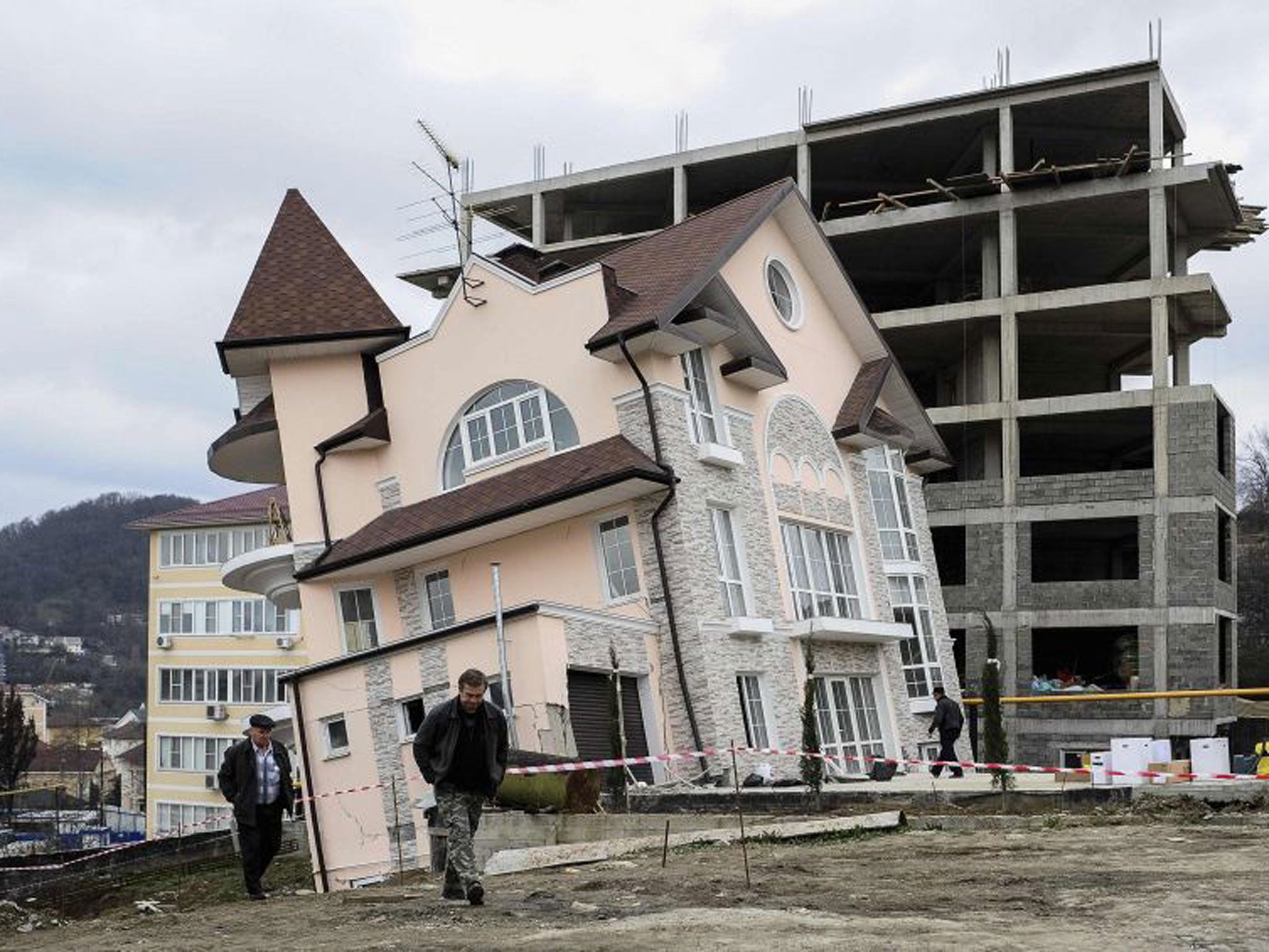 Men walk around a residential house that started leaning after a tunnel collapse in the Russian Black sea resort of Sochi