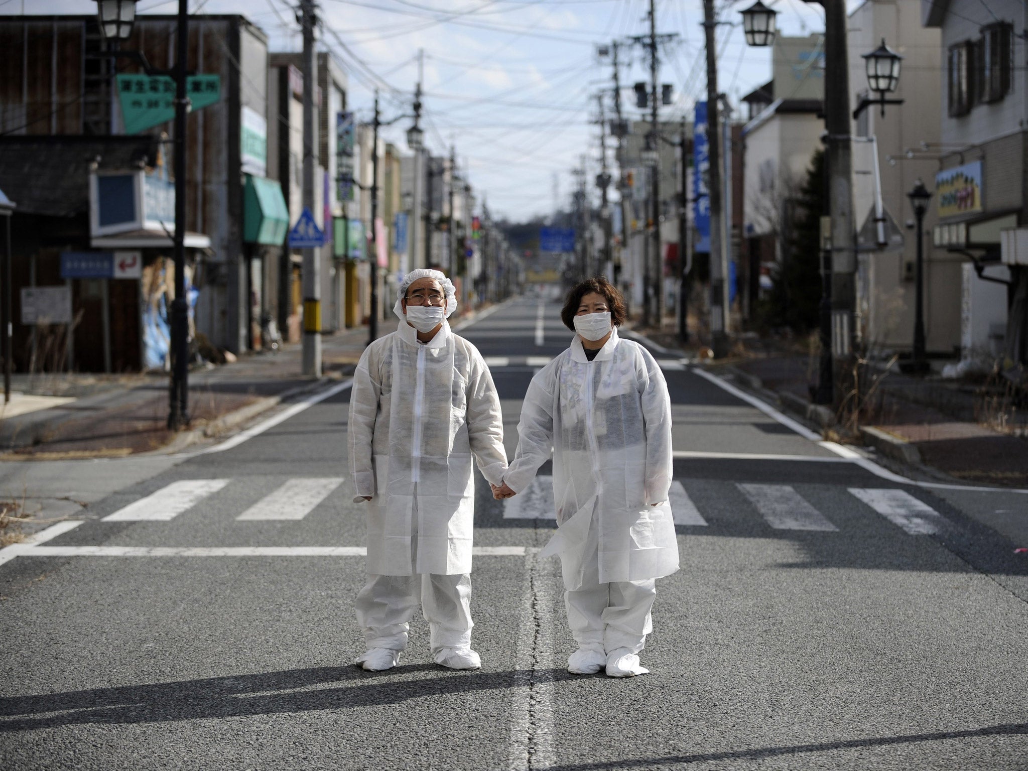 Wearing white protective masks and suits, Yuzo Mihara (L) and his wife Yuko pose for photographs on a deserted street in the town of Namie, Fukushima prefecture.