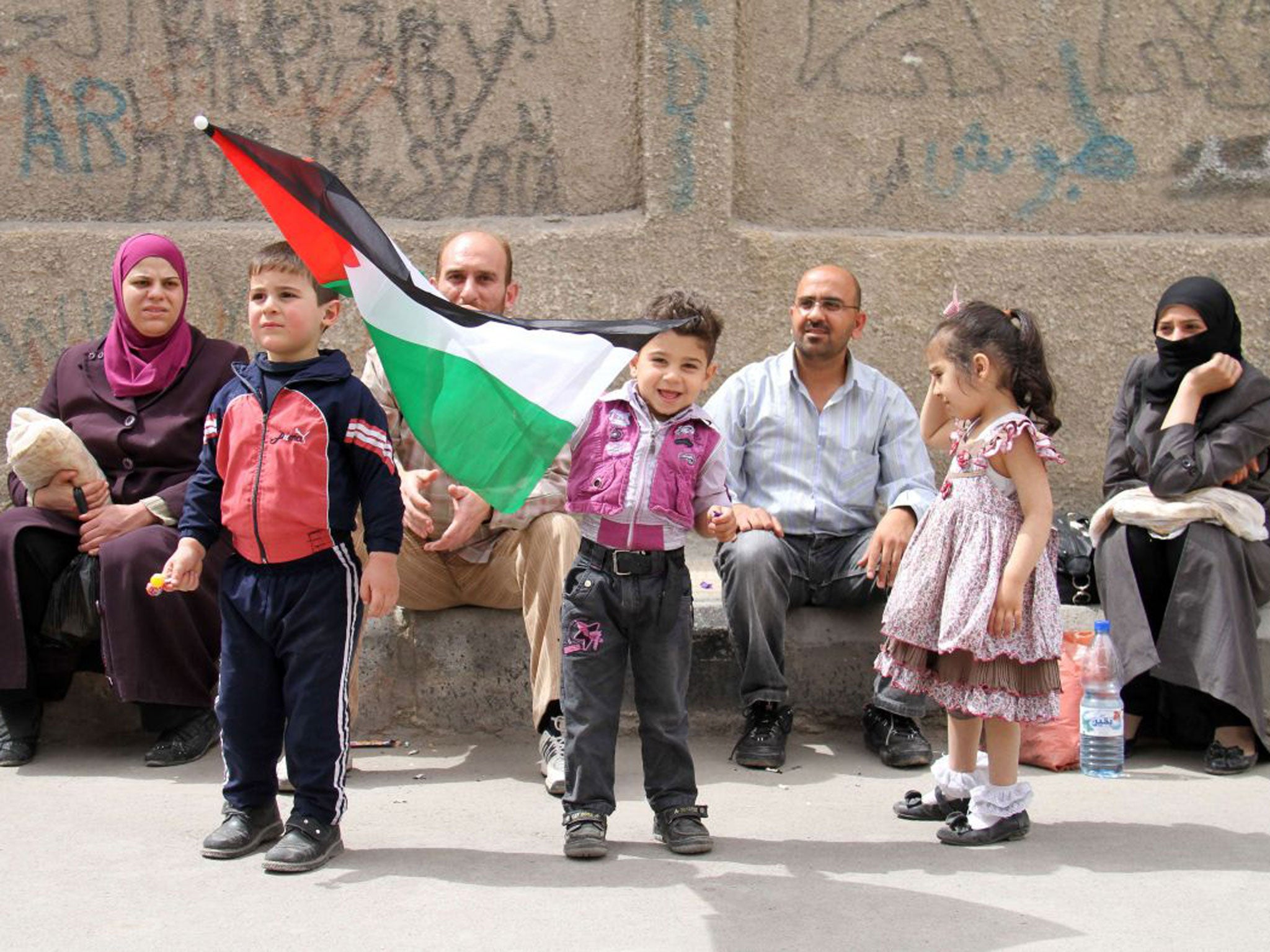 A Palestinian boy waves the national flag as he gathers with his family during a protest at the Yarmuk Palestinian refugee camp in the Syrian capital Damascus