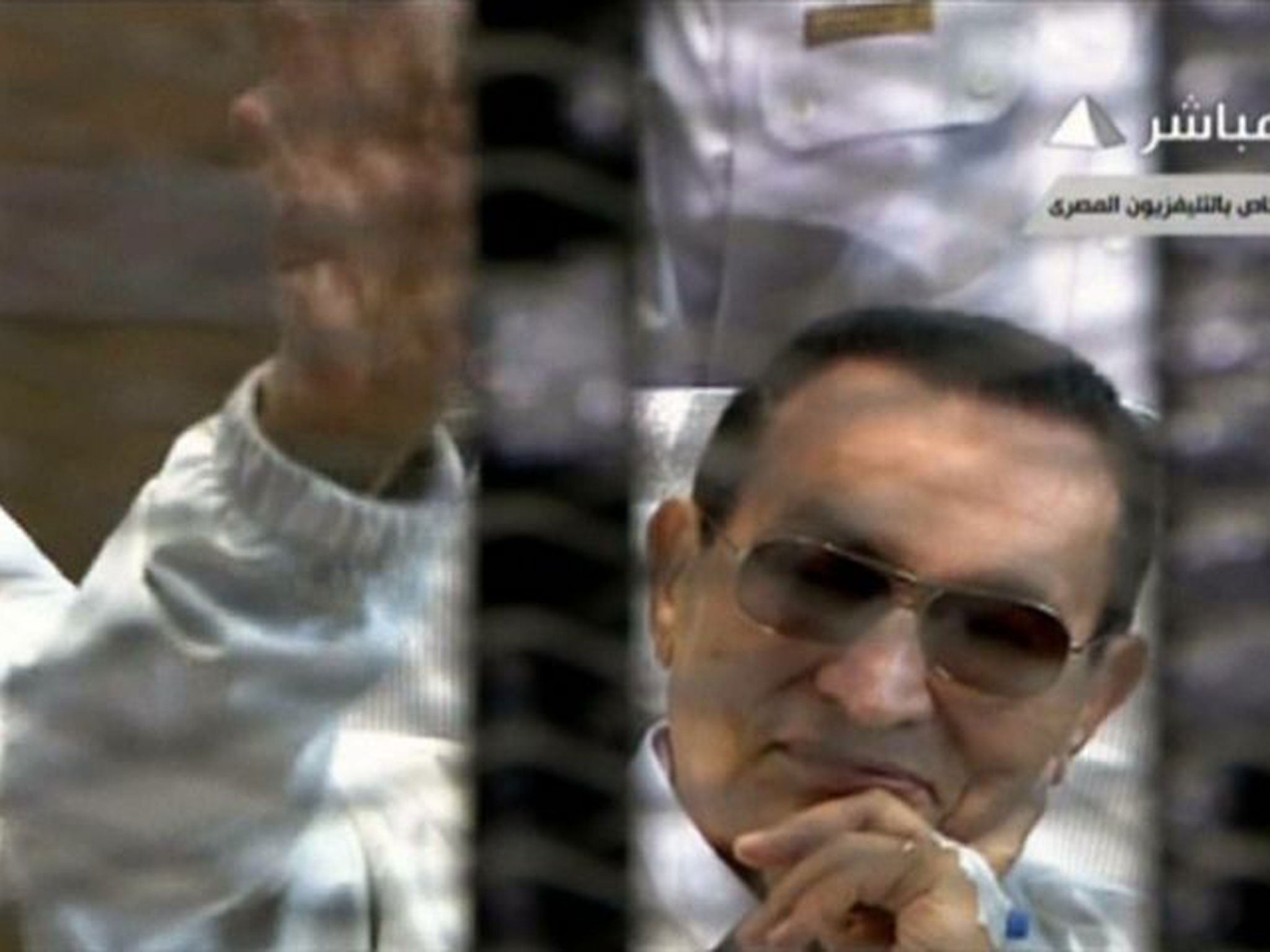 An image grab taken from Egyptian state TV shows ousted Egyptian president Hosni Mubarak waving from behind bars during his retrial at the Police Academy in Cairo