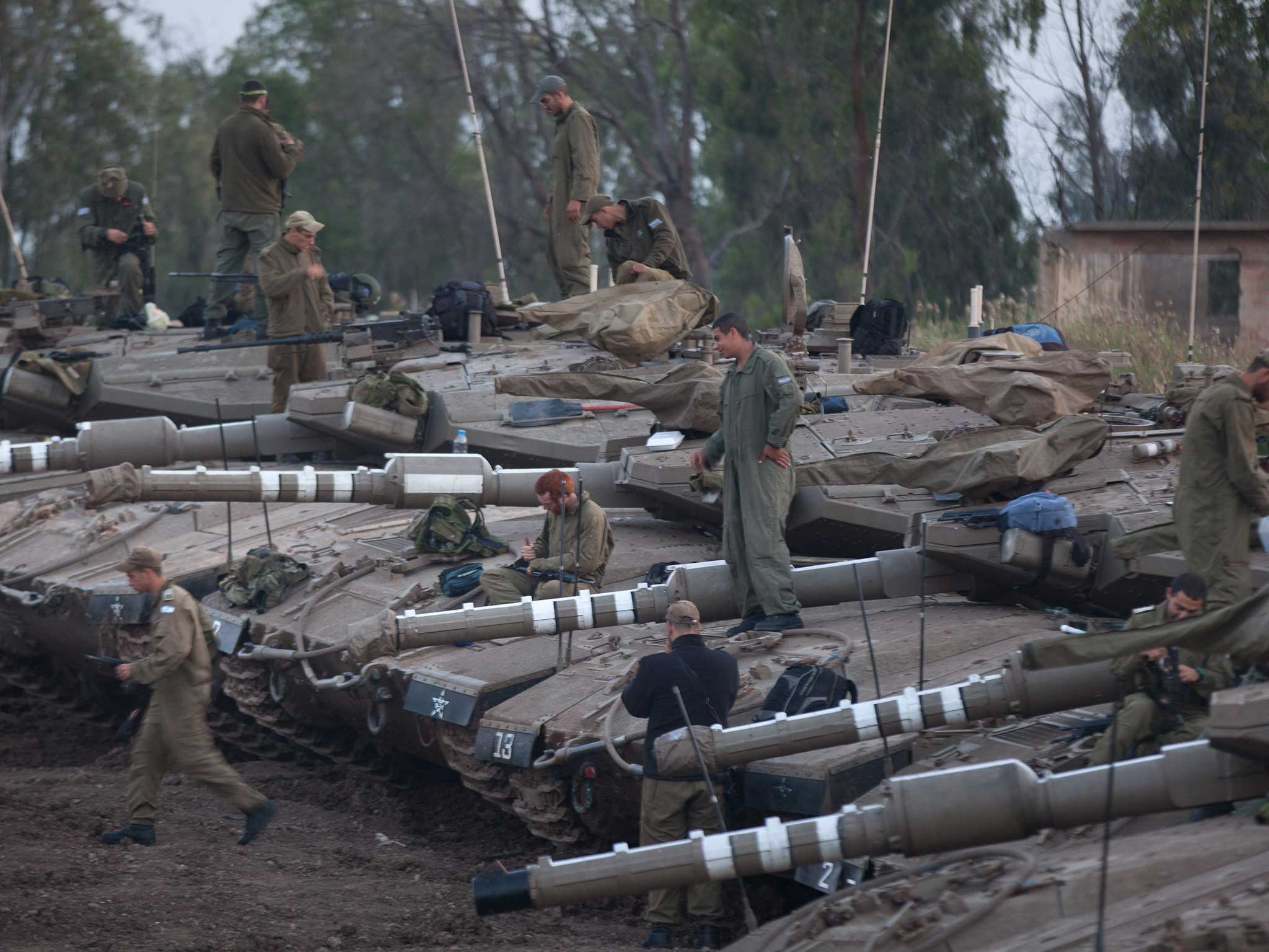 Israeli soldiers maintain their Merkava tanks at a deployment area near the border with Syria