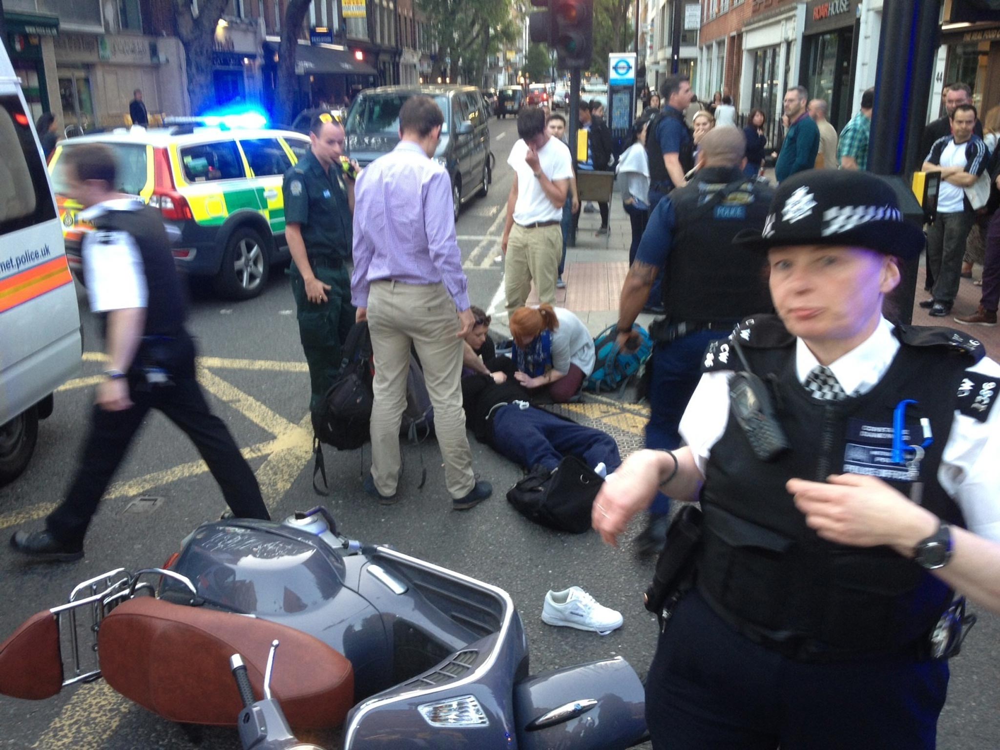 Police, medics and passers-by around a man who came off a moped at the corner of Goodge Street and Charlotte Street, London. He and another man were apprehended by police shortly after a raid at Selfridges
